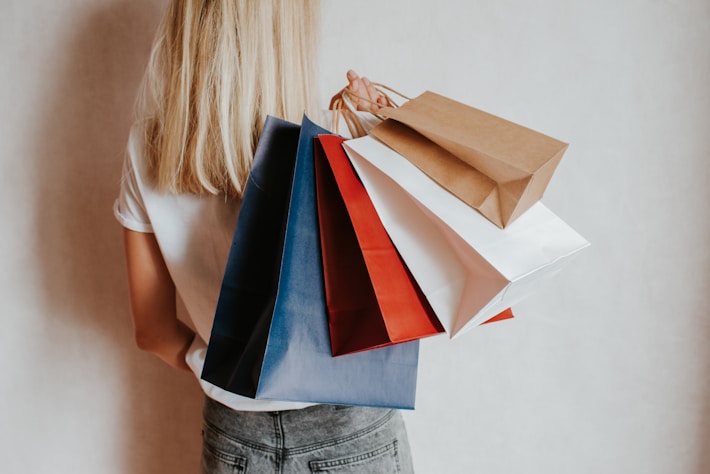 Woman holding colorful shopping bags against a wall.