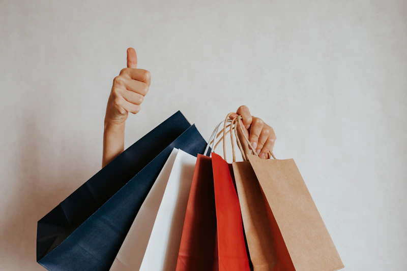 Person holding colourful shopping bags with a thumbs up