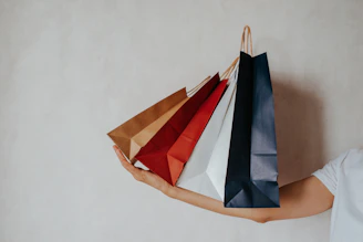 Hand holding colorful shopping bags against a light wall.