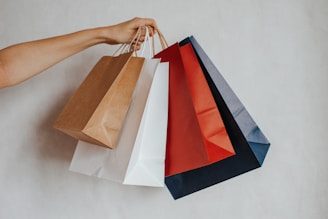 Hand holding colorful shopping bags against a light background