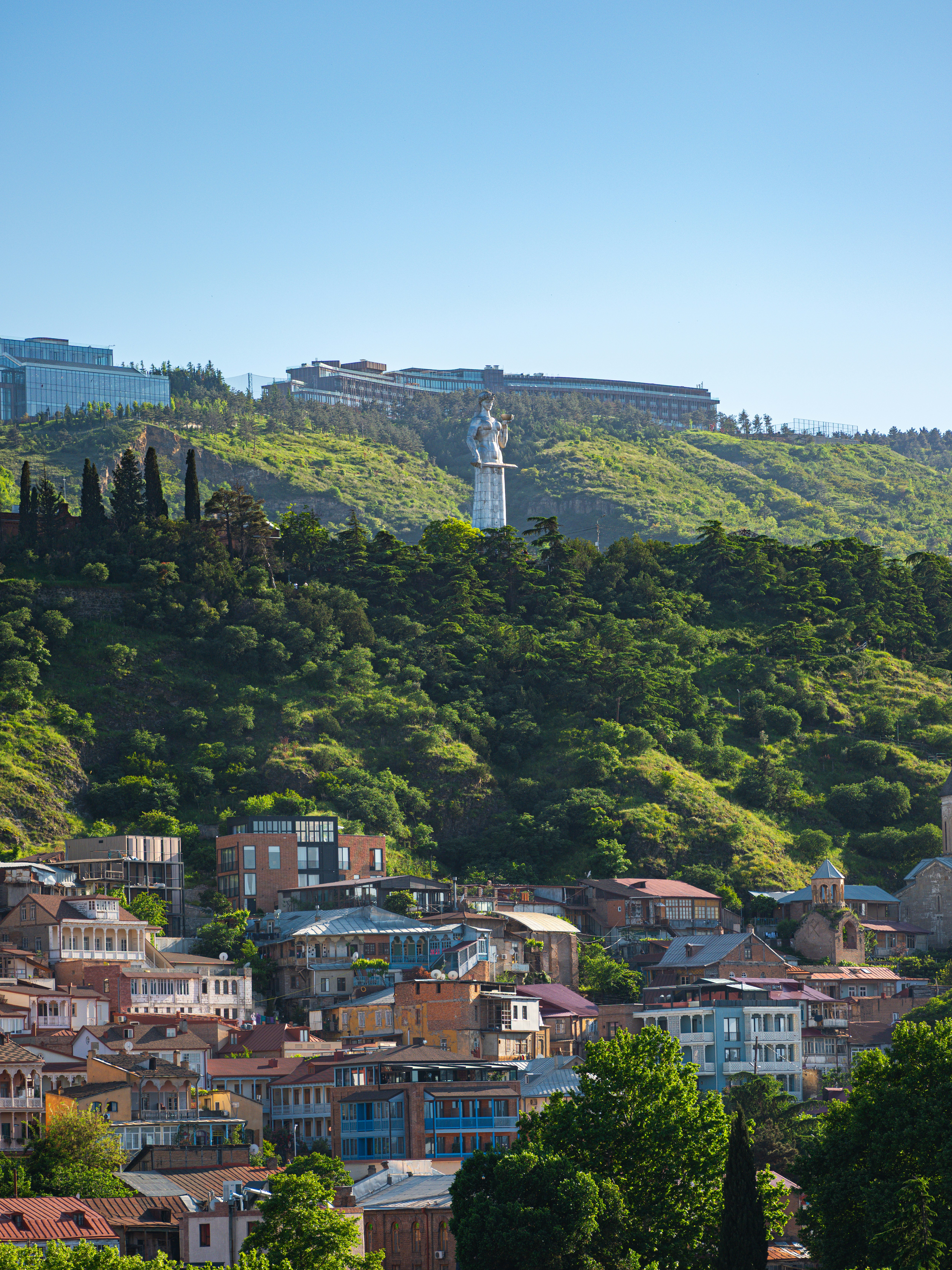 Cityscape with statue on a green hill above buildings below