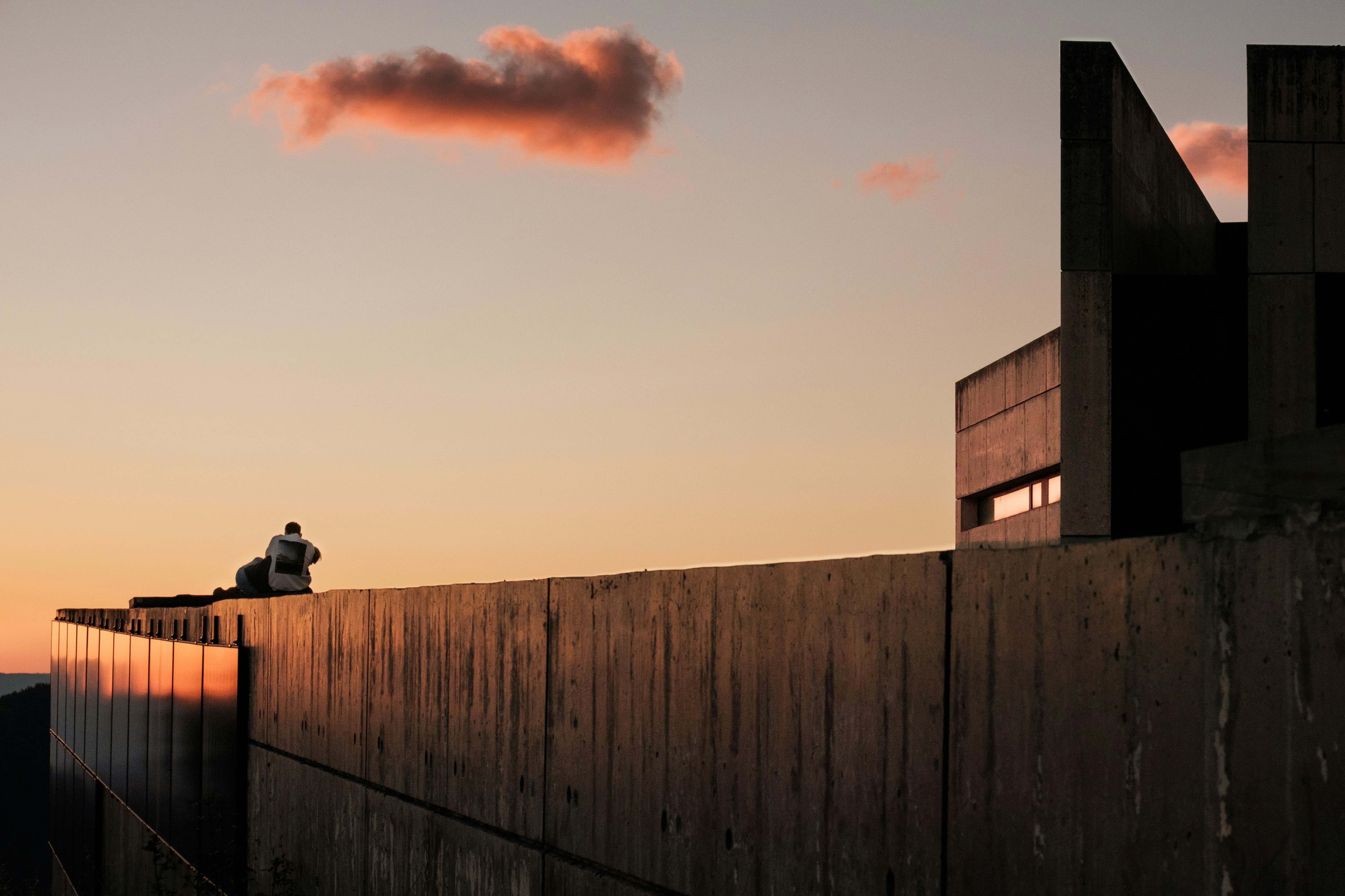 Person sitting on concrete wall at sunset