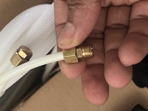 Hand holding a brass fitting on a white tube