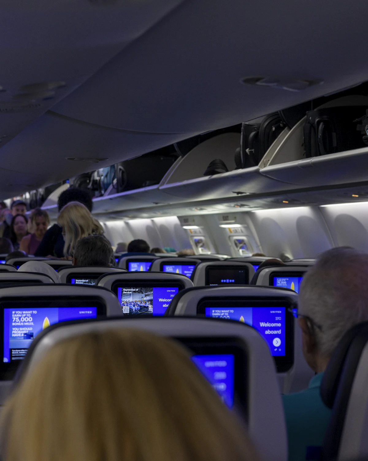 Interior of an airplane cabin with passengers and seat-back screens