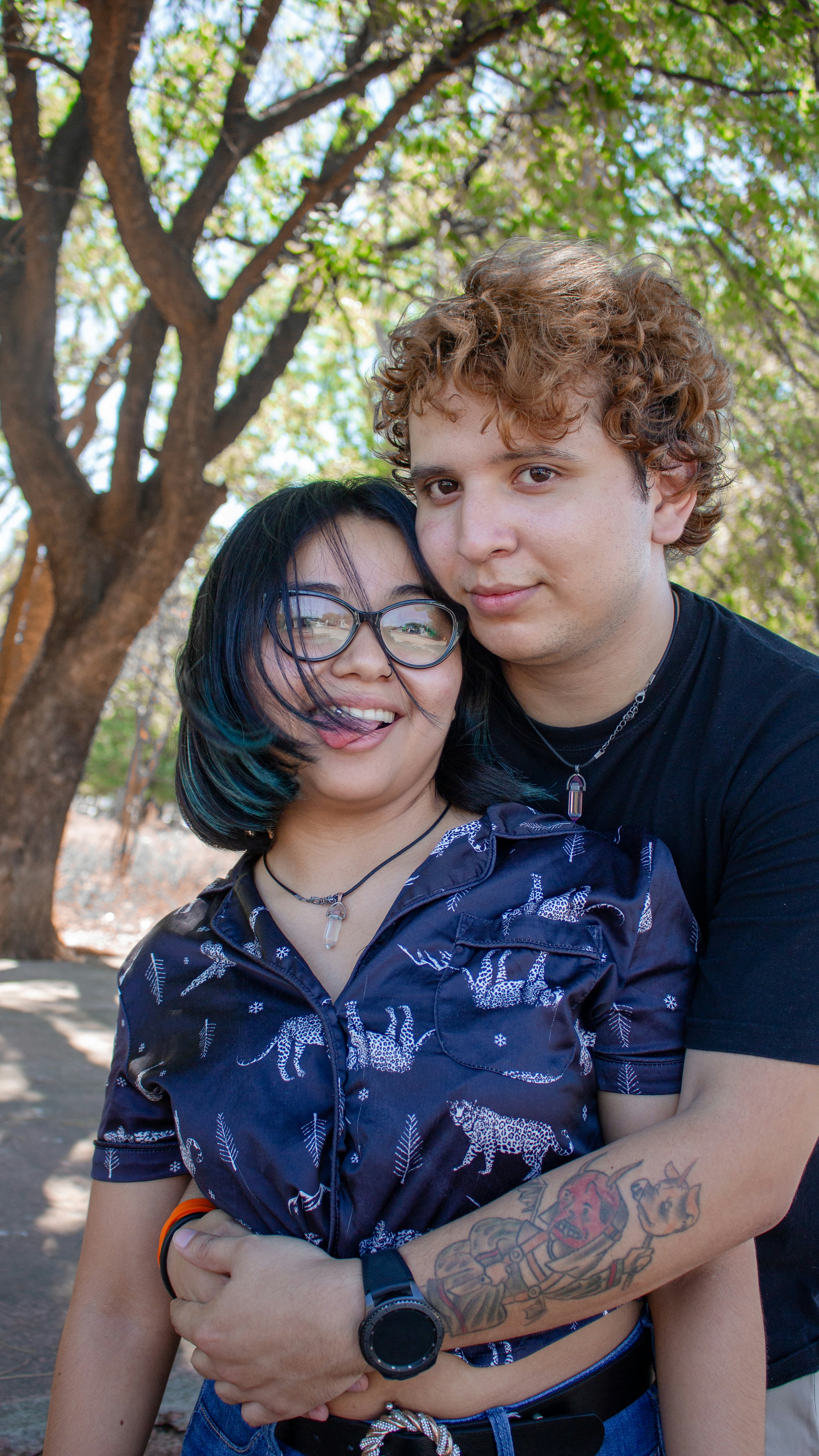 Una pareja abrazándose al aire libre bajo un árbol.