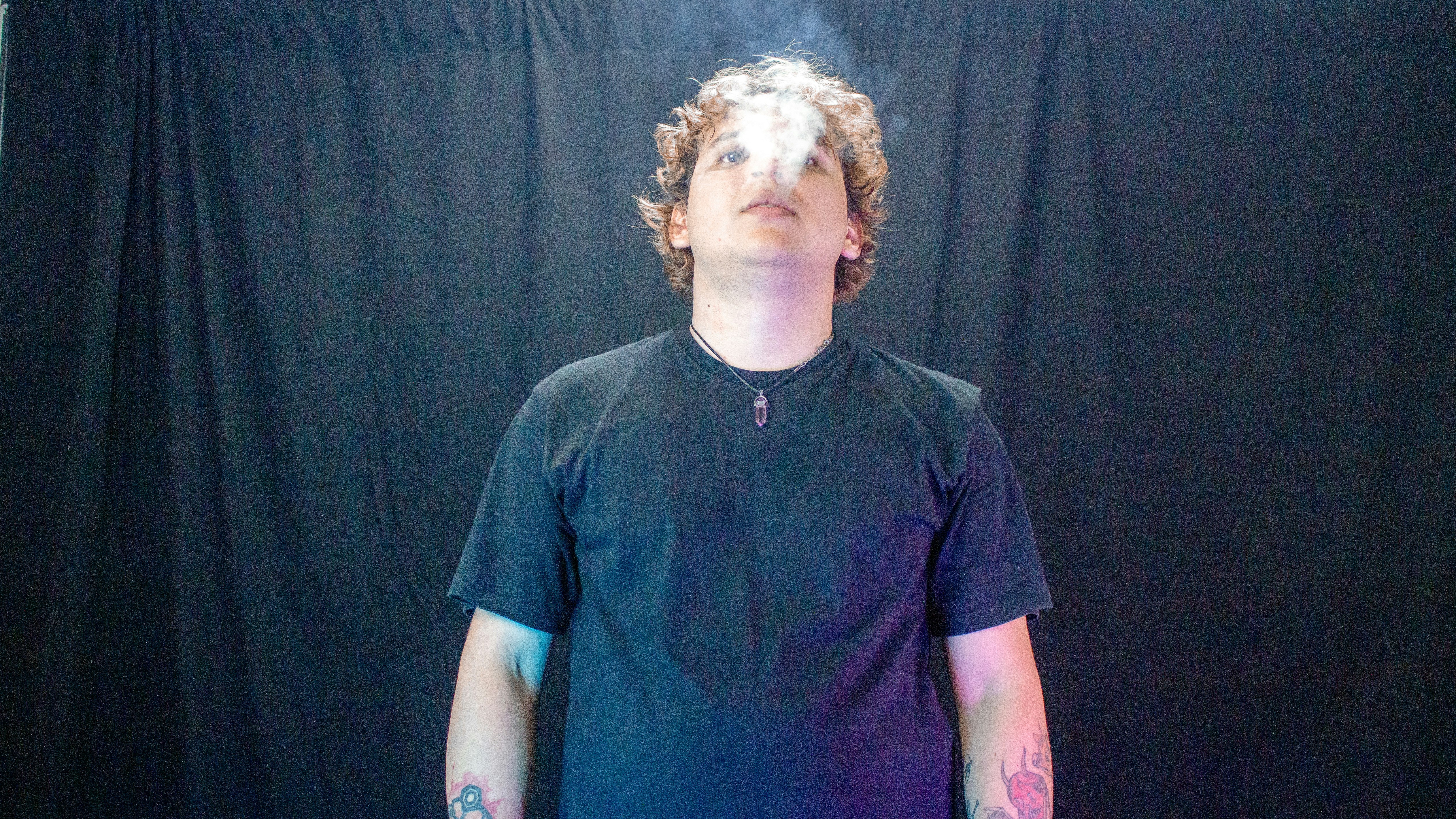 Young man exhaling smoke against a black backdrop.