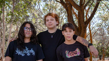 Three young people stand together outdoors.