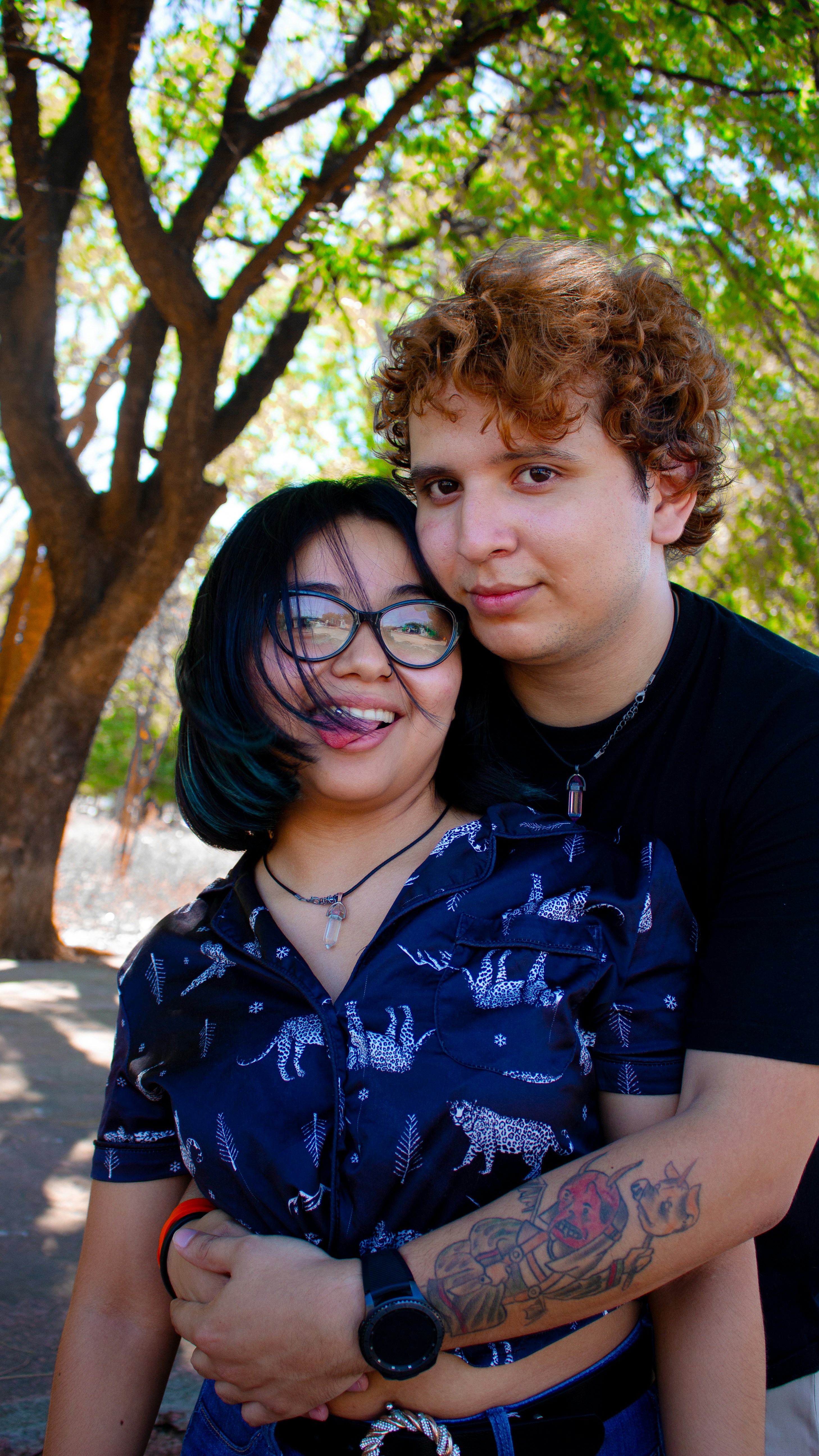 Un jeune couple s’embrasse à l’extérieur sous un arbre.