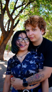 A young couple embraces outdoors under a tree.