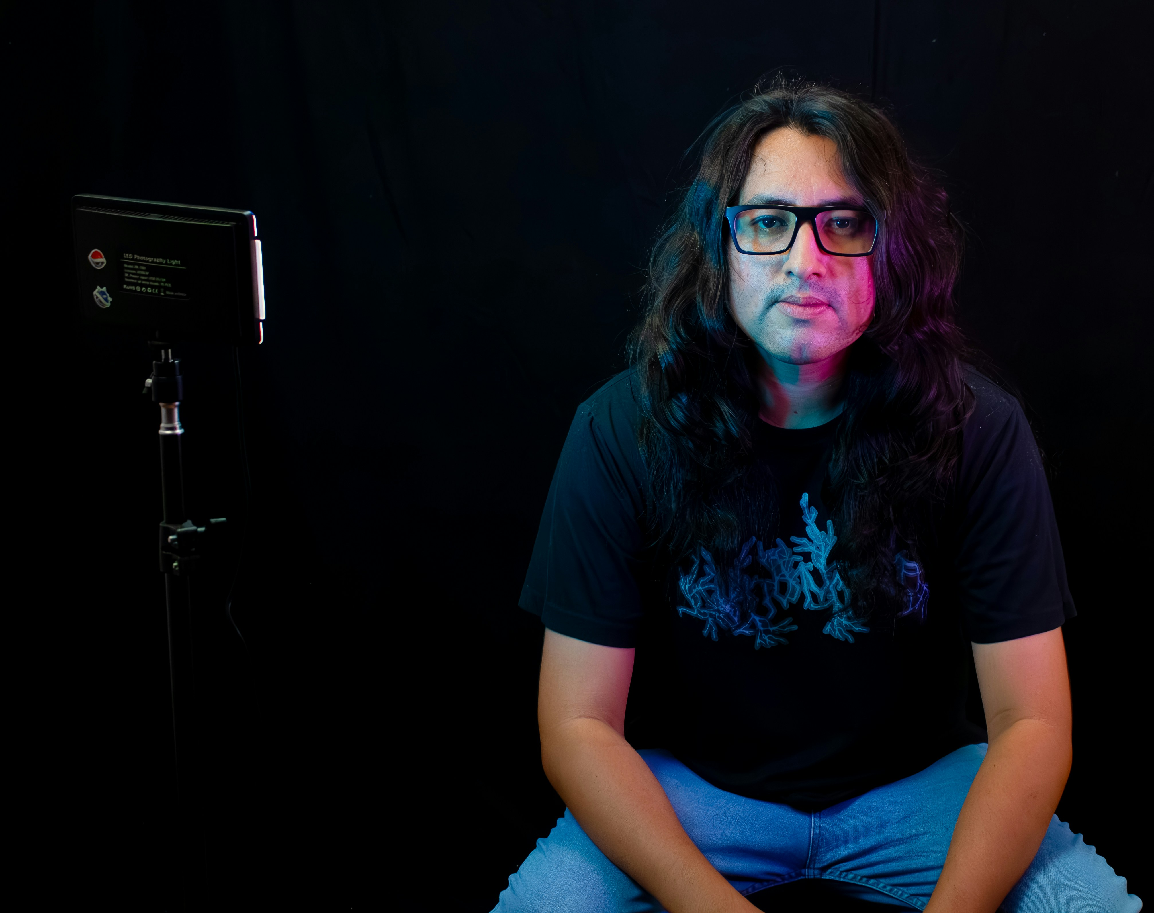 Man with glasses and long hair against black background.