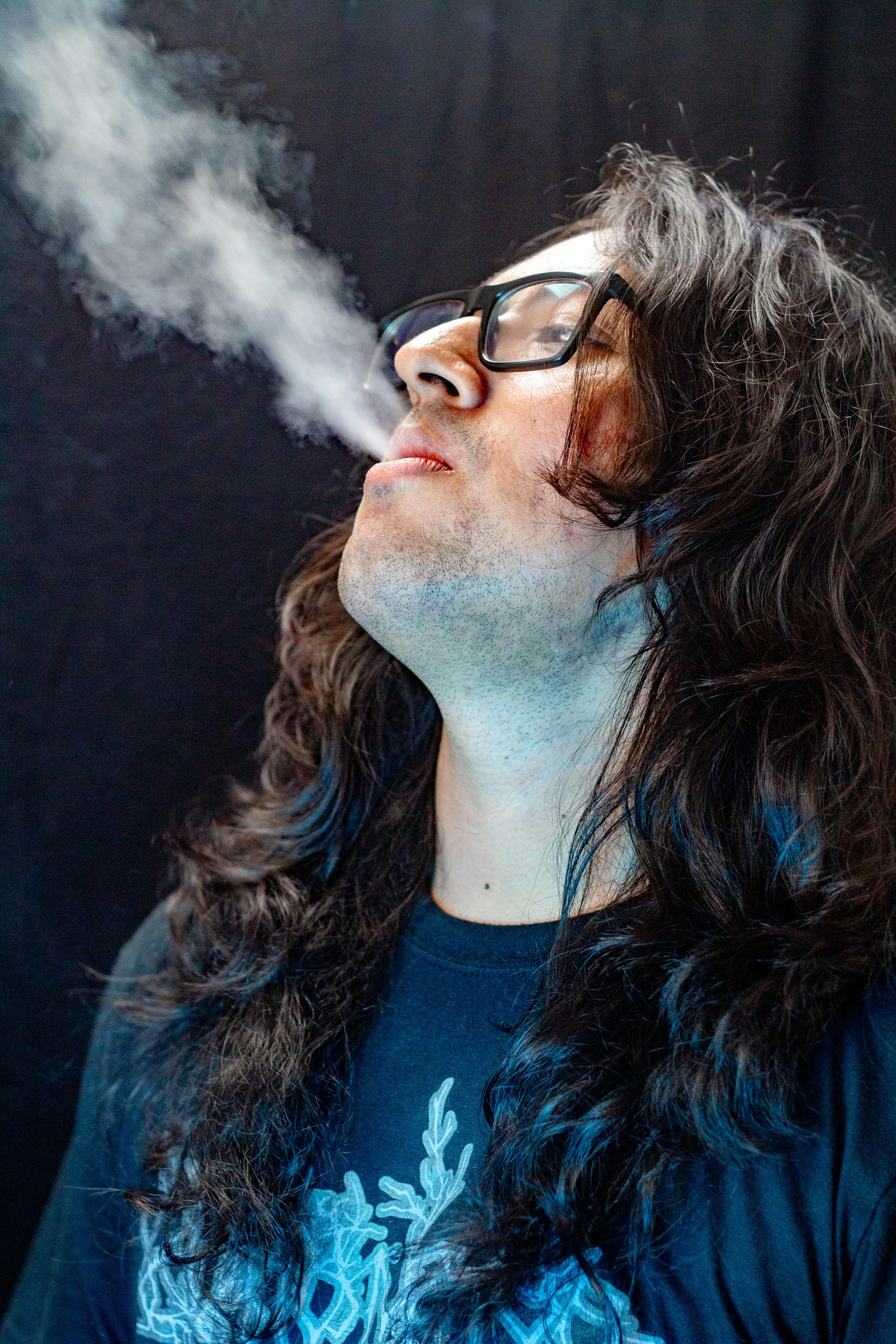 Man with long hair exhales smoke through his mouth