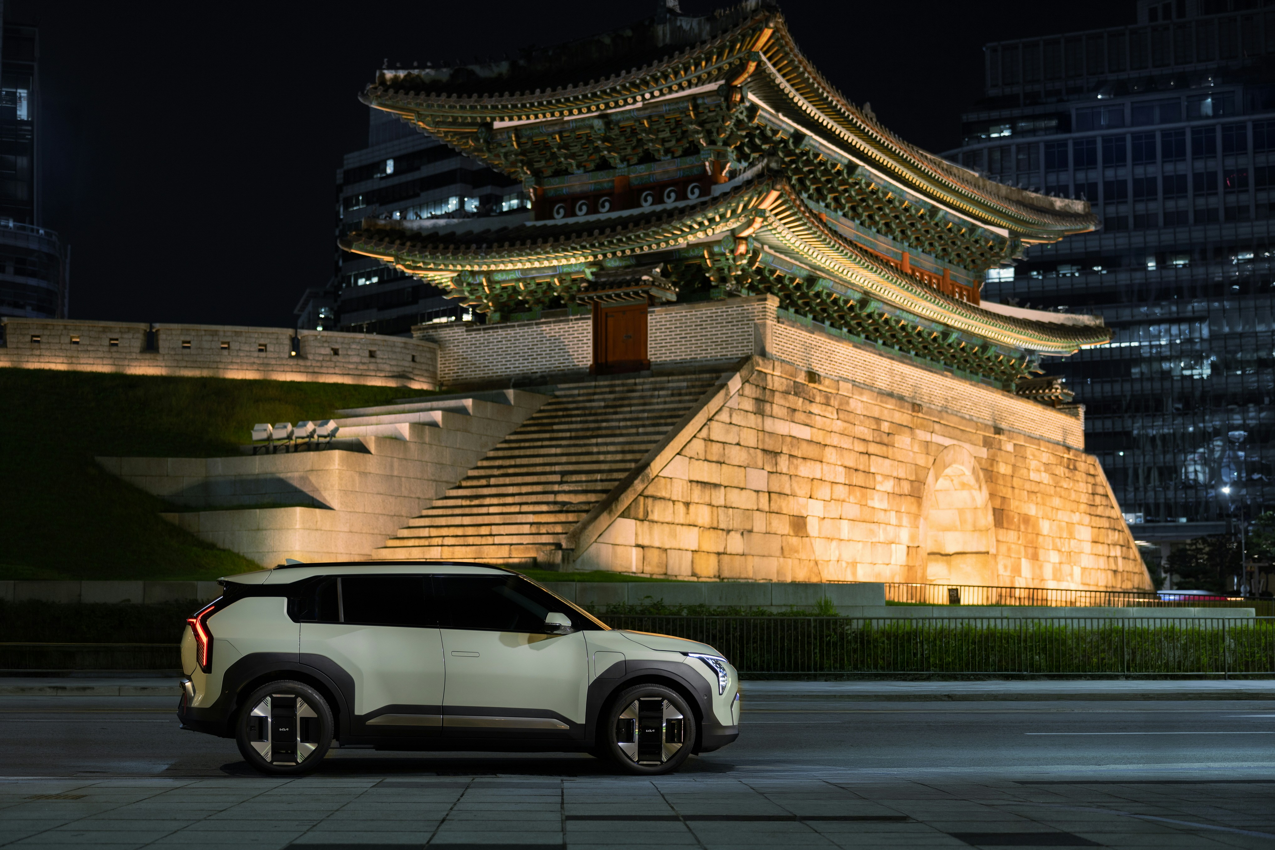 Modern car parked near illuminated ancient gate at night