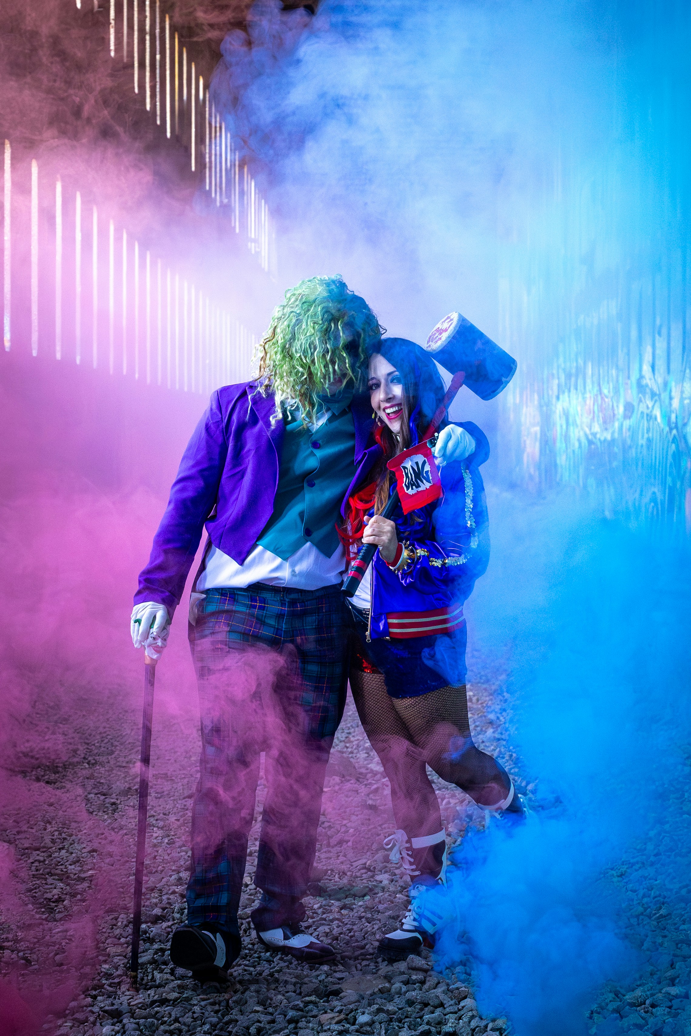 Cosplayer berpakaian seperti joker dan harley quinn berpelukan dalam asap.
