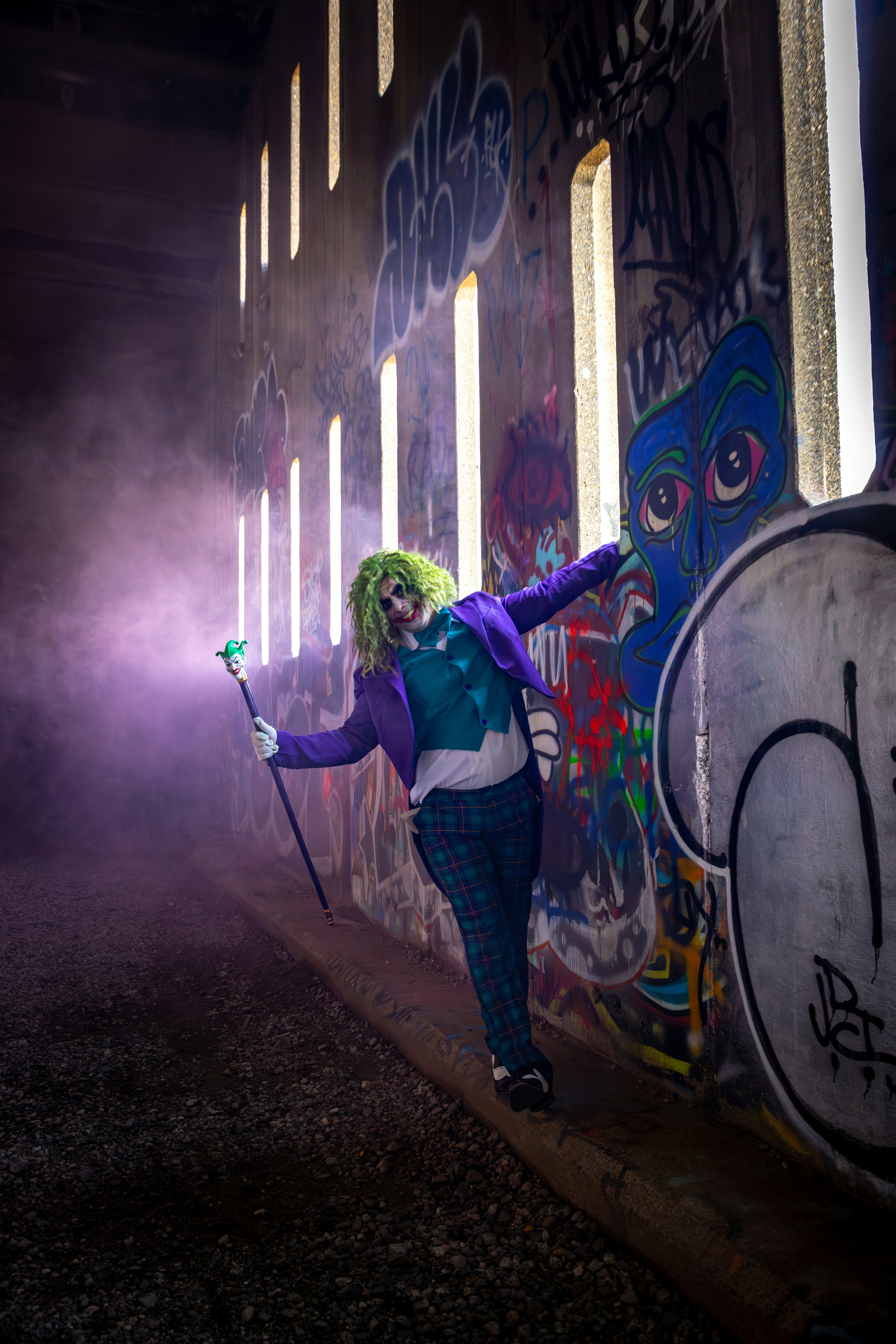 Person in joker costume with purple smoke and cane.