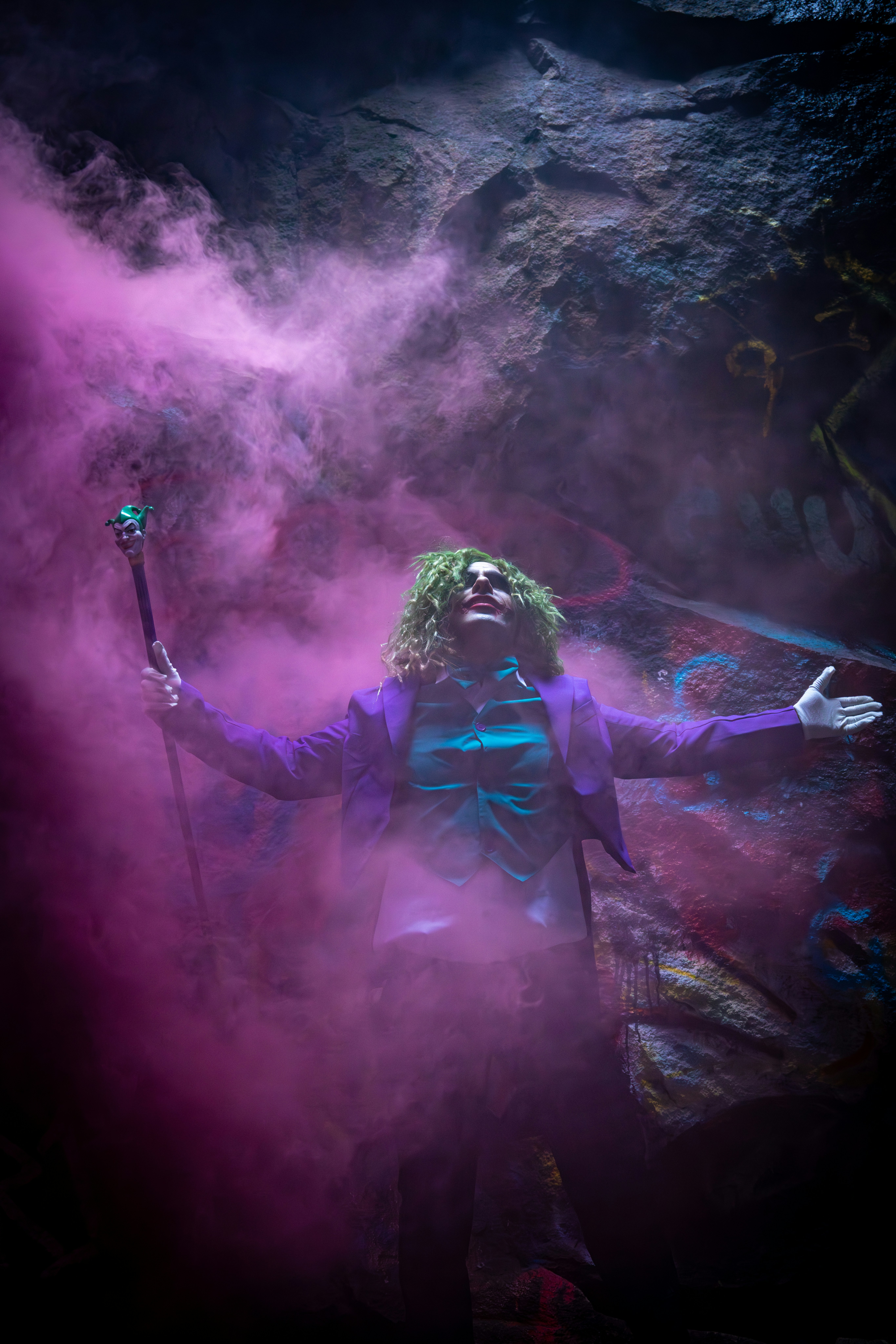 Man in purple suit with green hair in pink smoke.