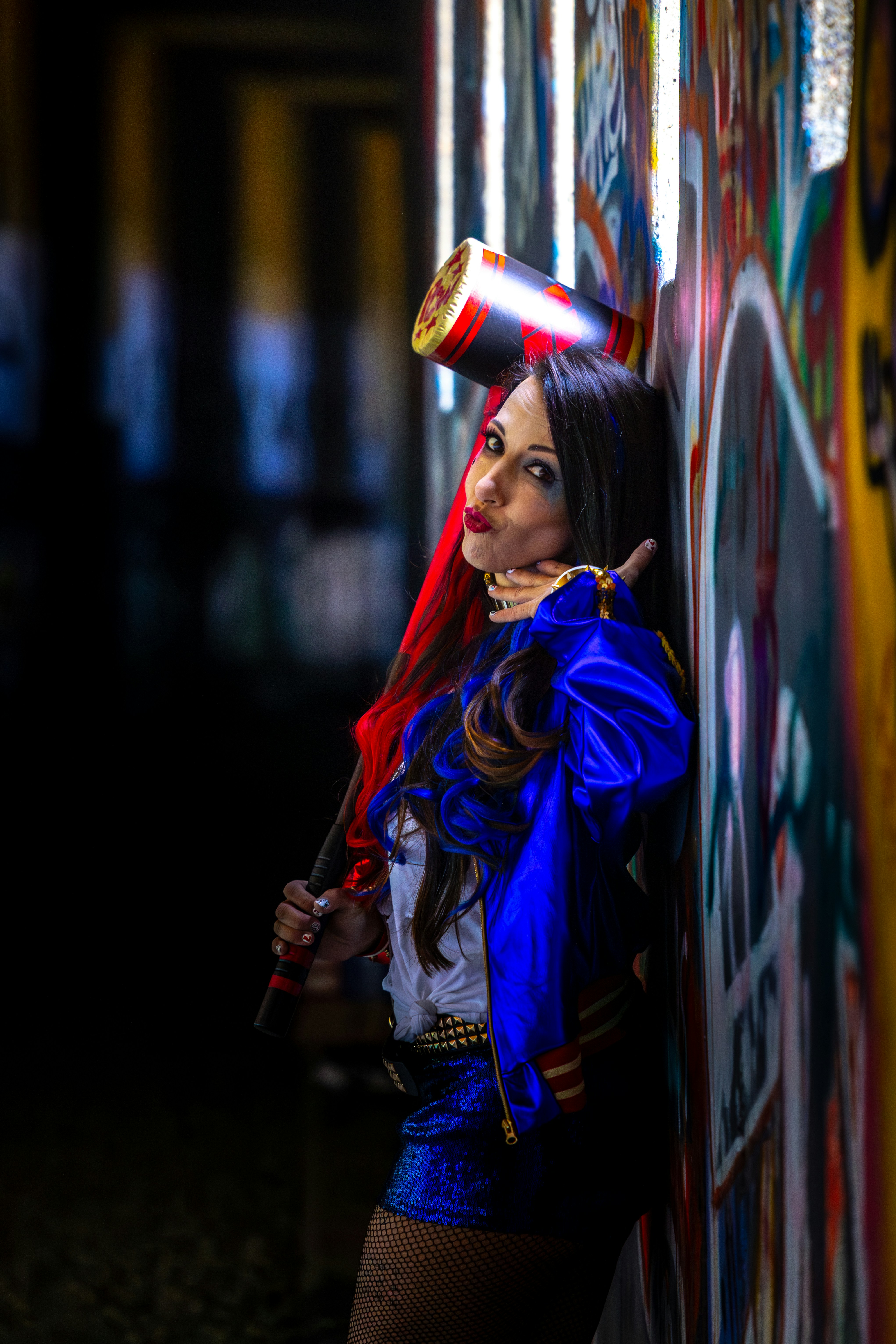 Woman in harley quinn costume with mallet leans on wall