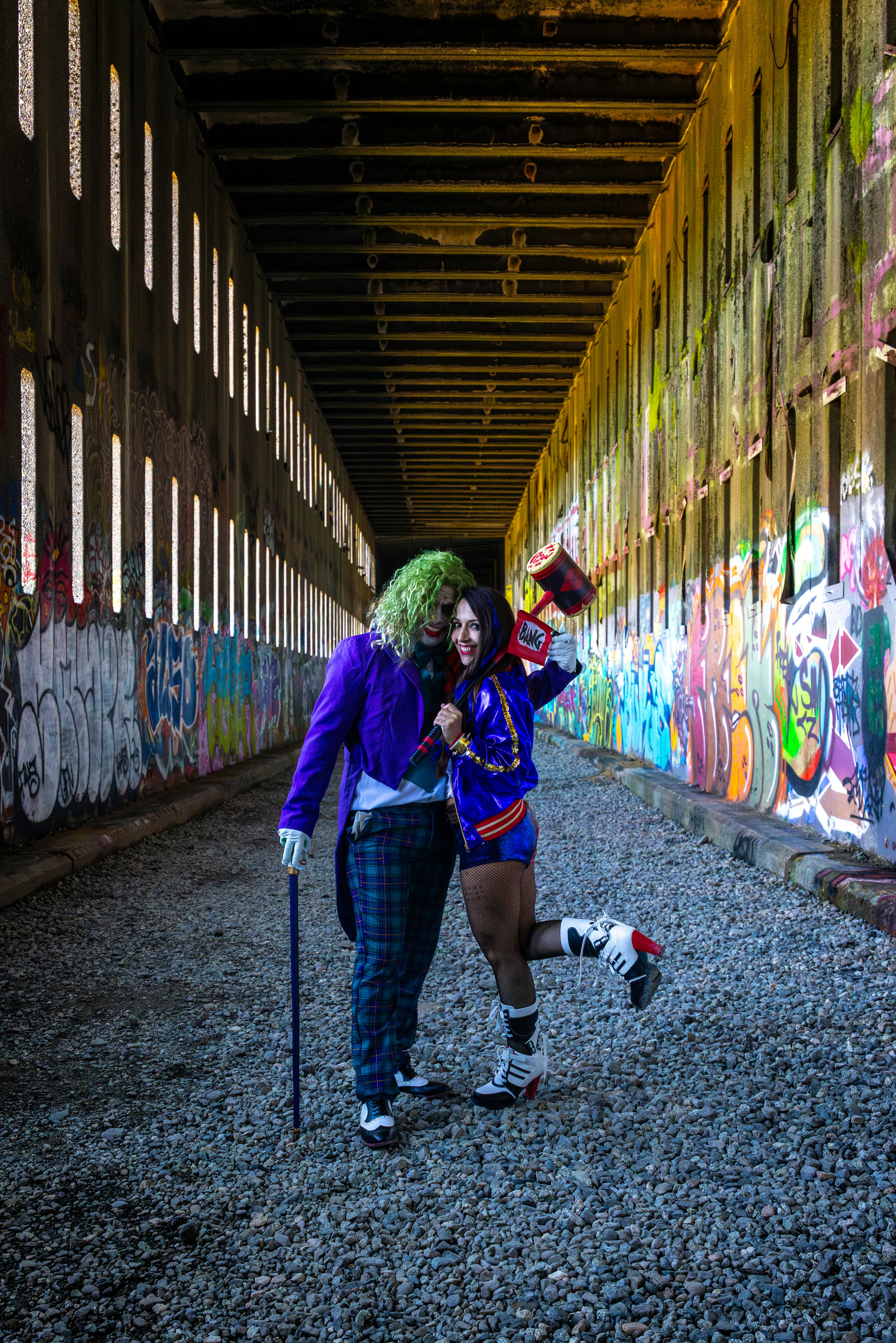 Pasangan dengan kostum joker dan harley quinn berpelukan di bawah jembatan.