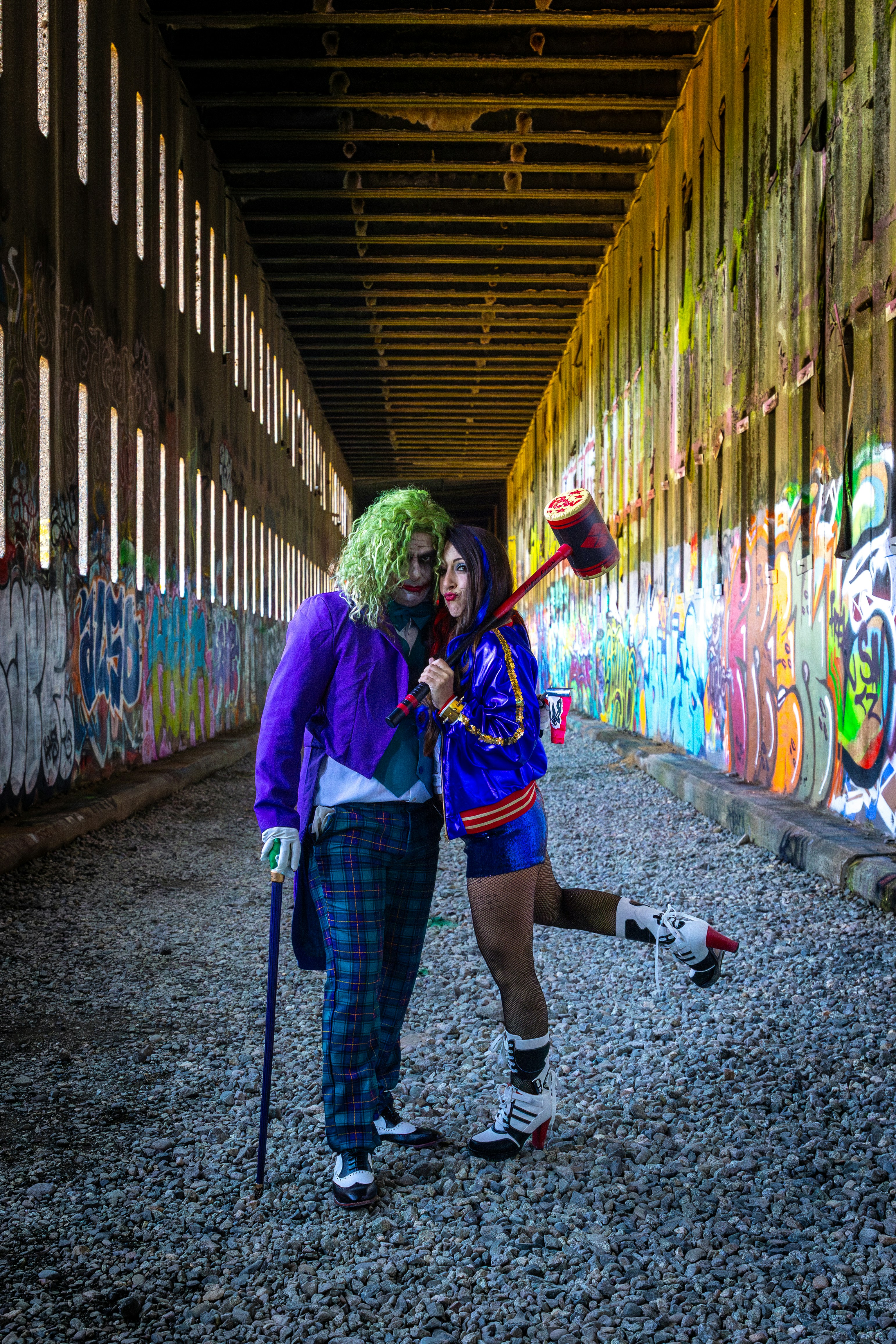 Cosplayers dressed as joker and harley quinn in alley.