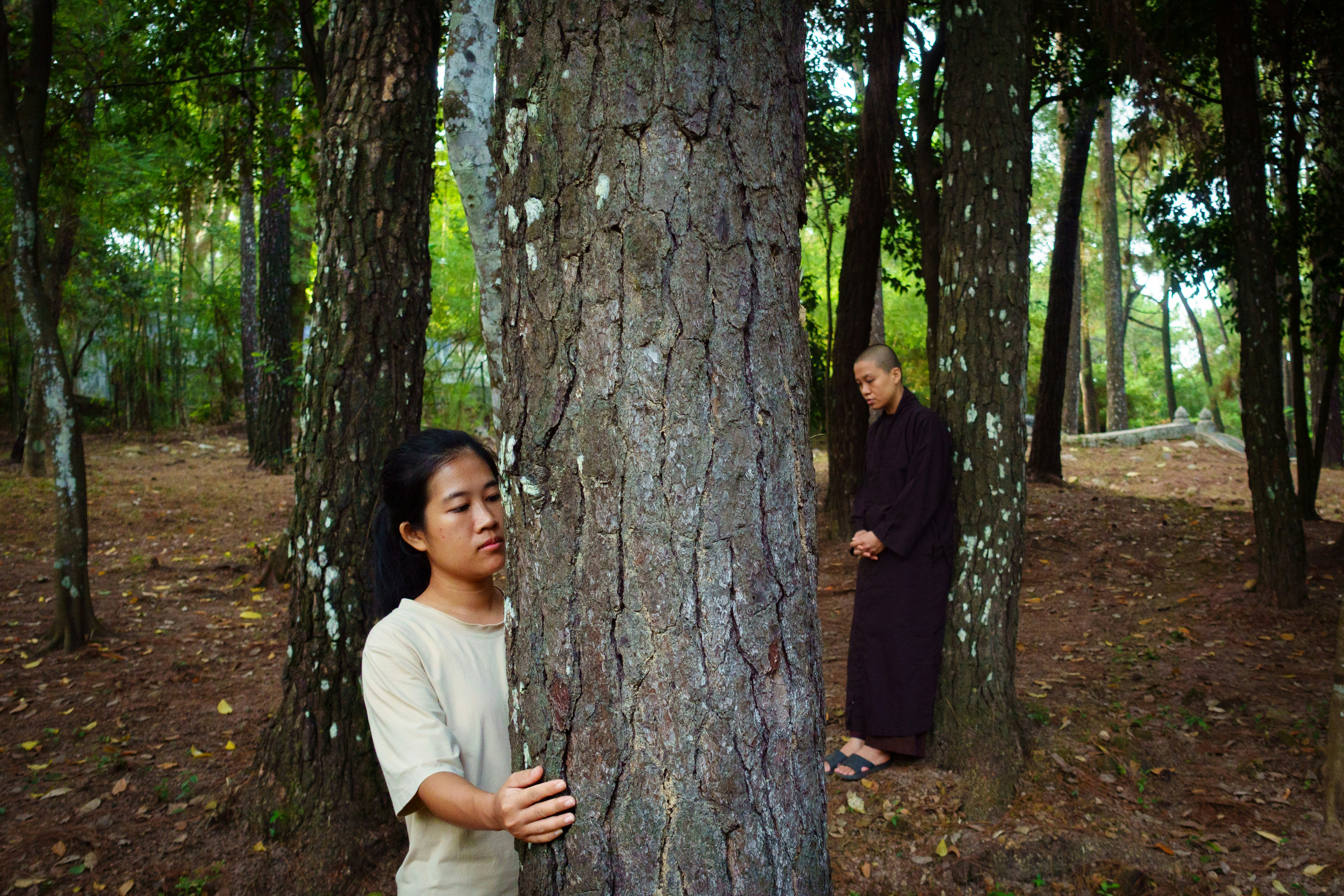 Woman peeking from behind tree, monk in background