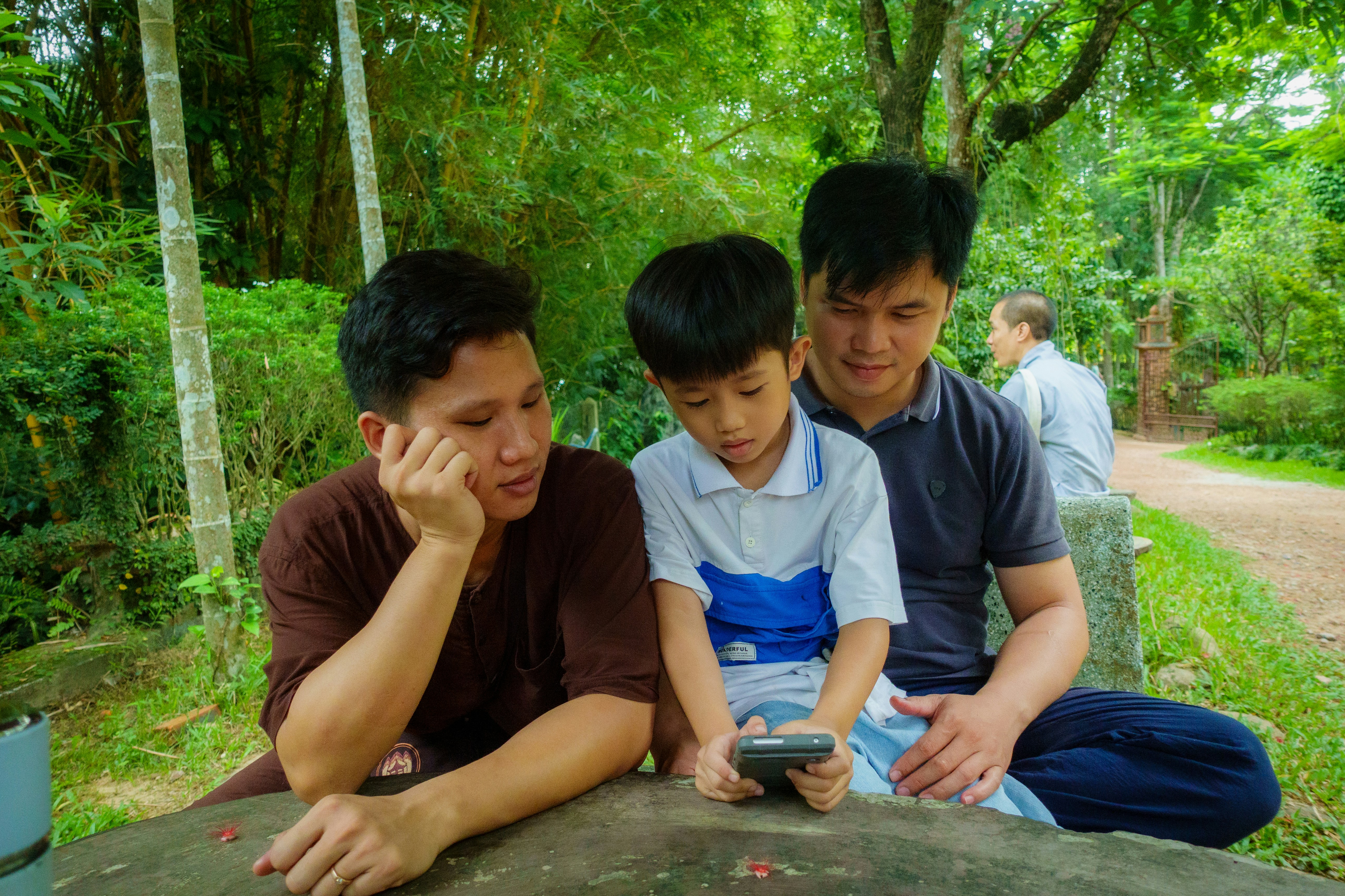 Two men and a boy look at a phone.