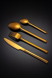 Set of four gold cutlery pieces on black background