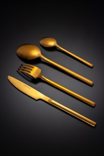Set of four gold cutlery pieces on black background