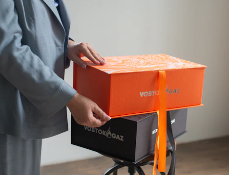 Hands opening a bright orange gift box with ribbon