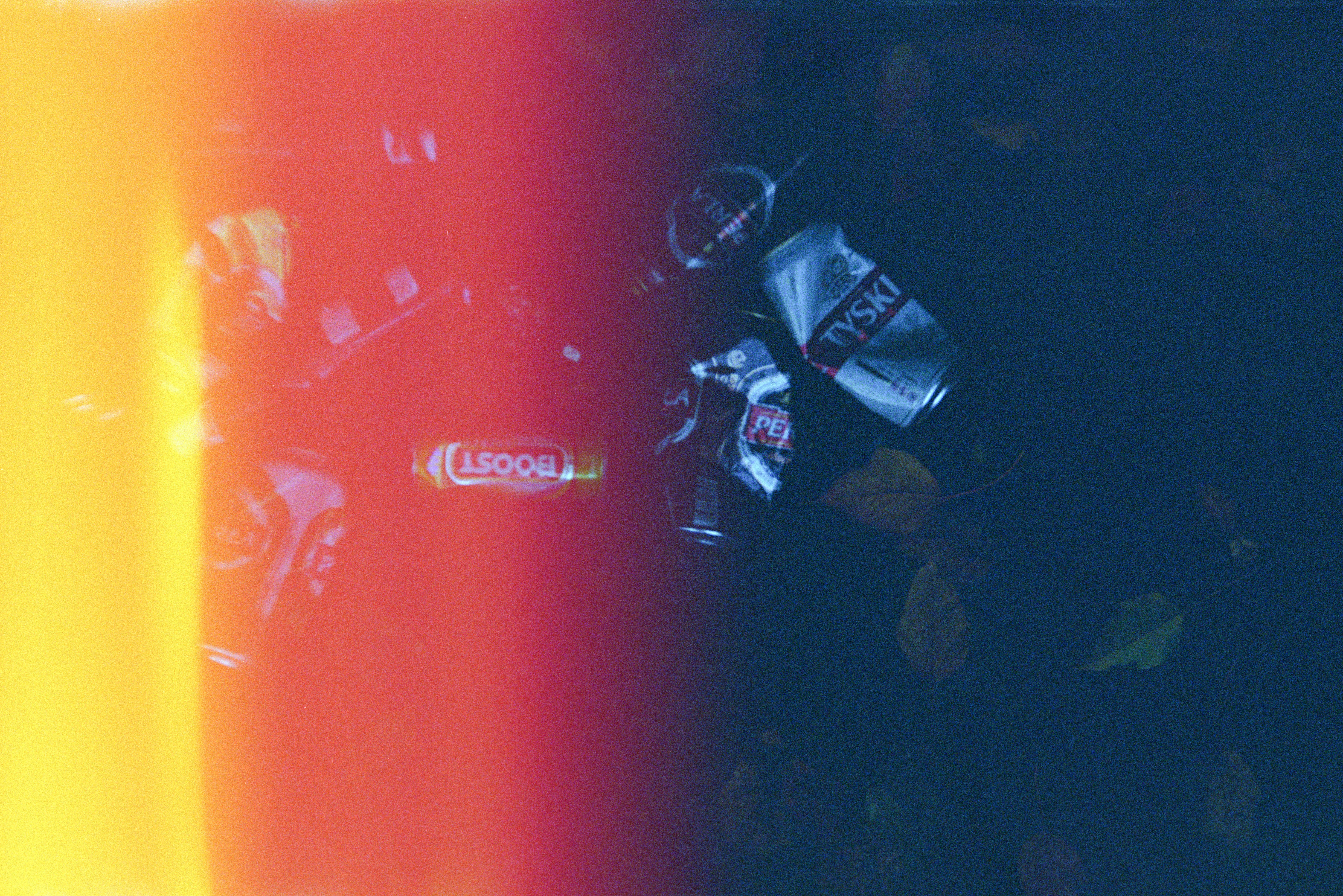 Discarded aluminum cans litter a dark, leaf-strewn ground.