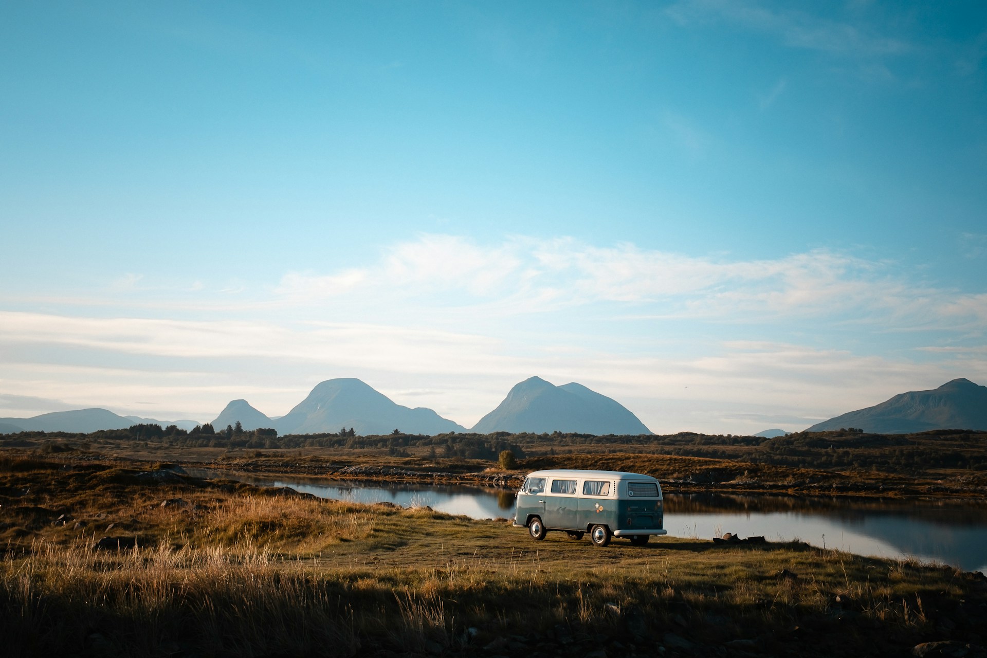Vintage van parked by a calm lake near mountains.