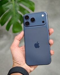 Hand holding a dark blue smartphone with camera lenses.
