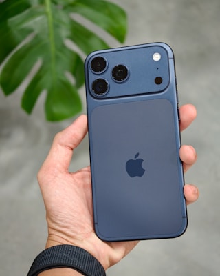 Hand holding a dark blue smartphone with camera lenses.