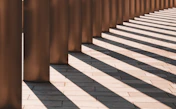 Bronze columns casting long shadows on paved ground