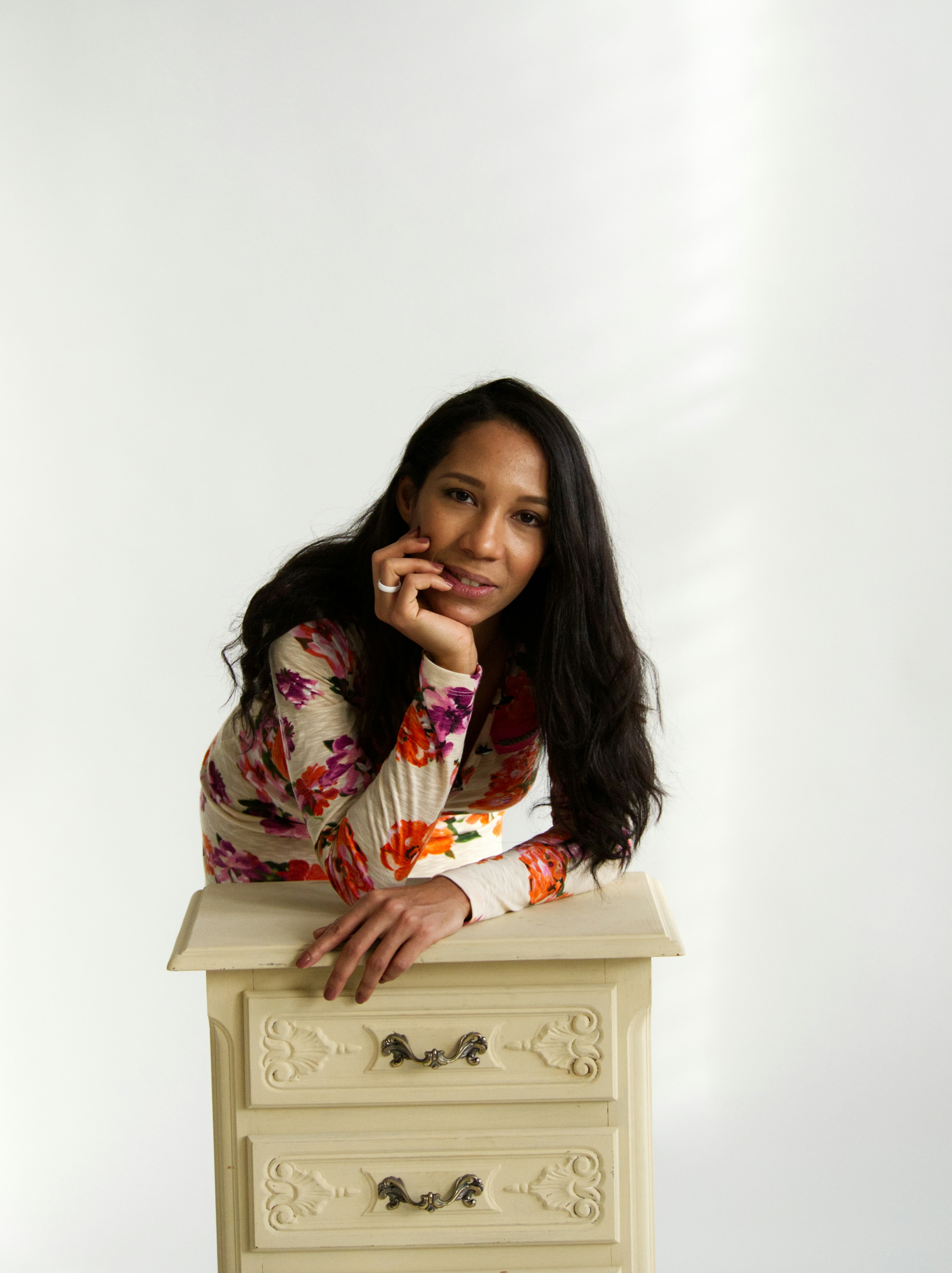 Woman in floral dress leans on antique dresser