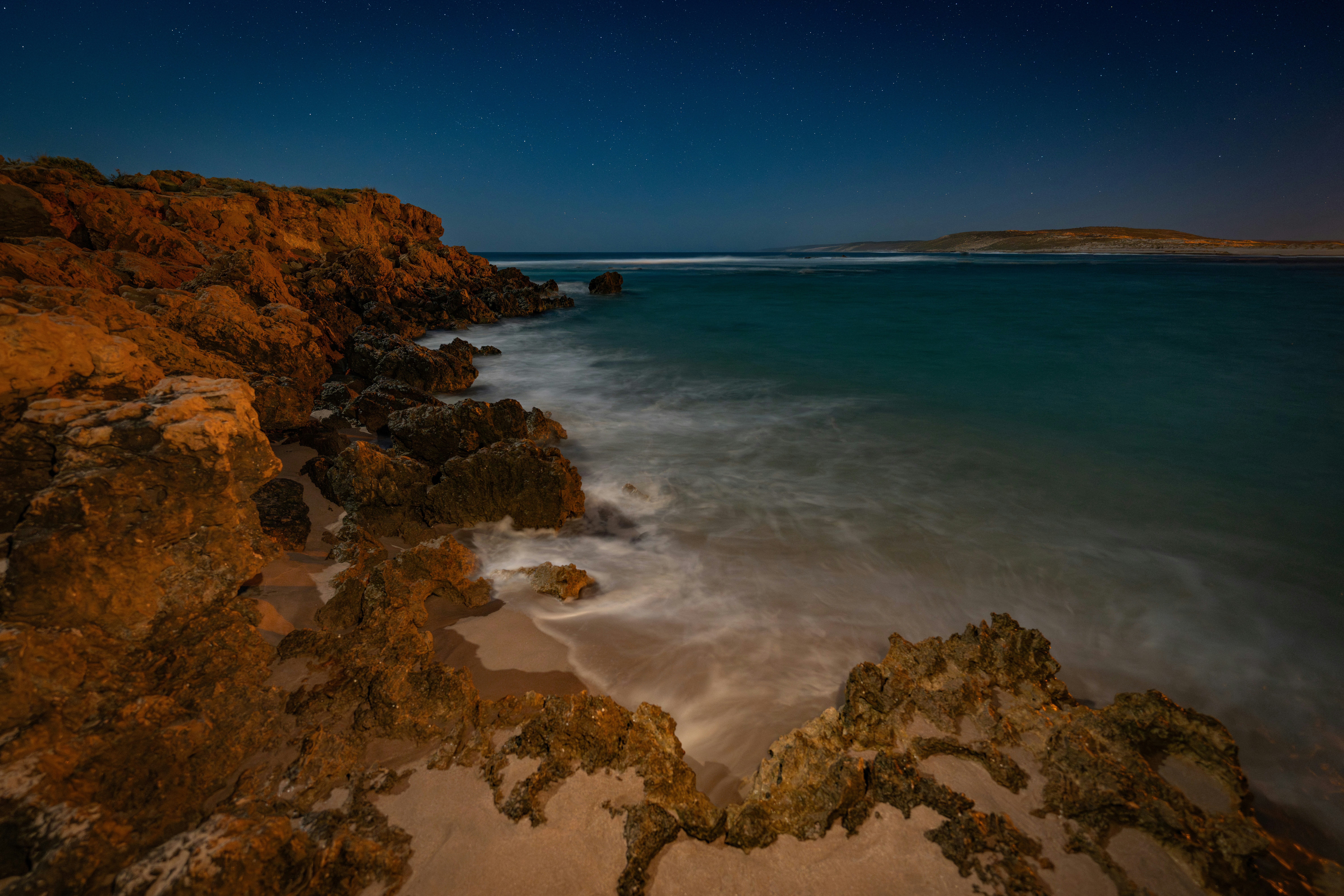 Rocky coastline with waves crashing under starry sky