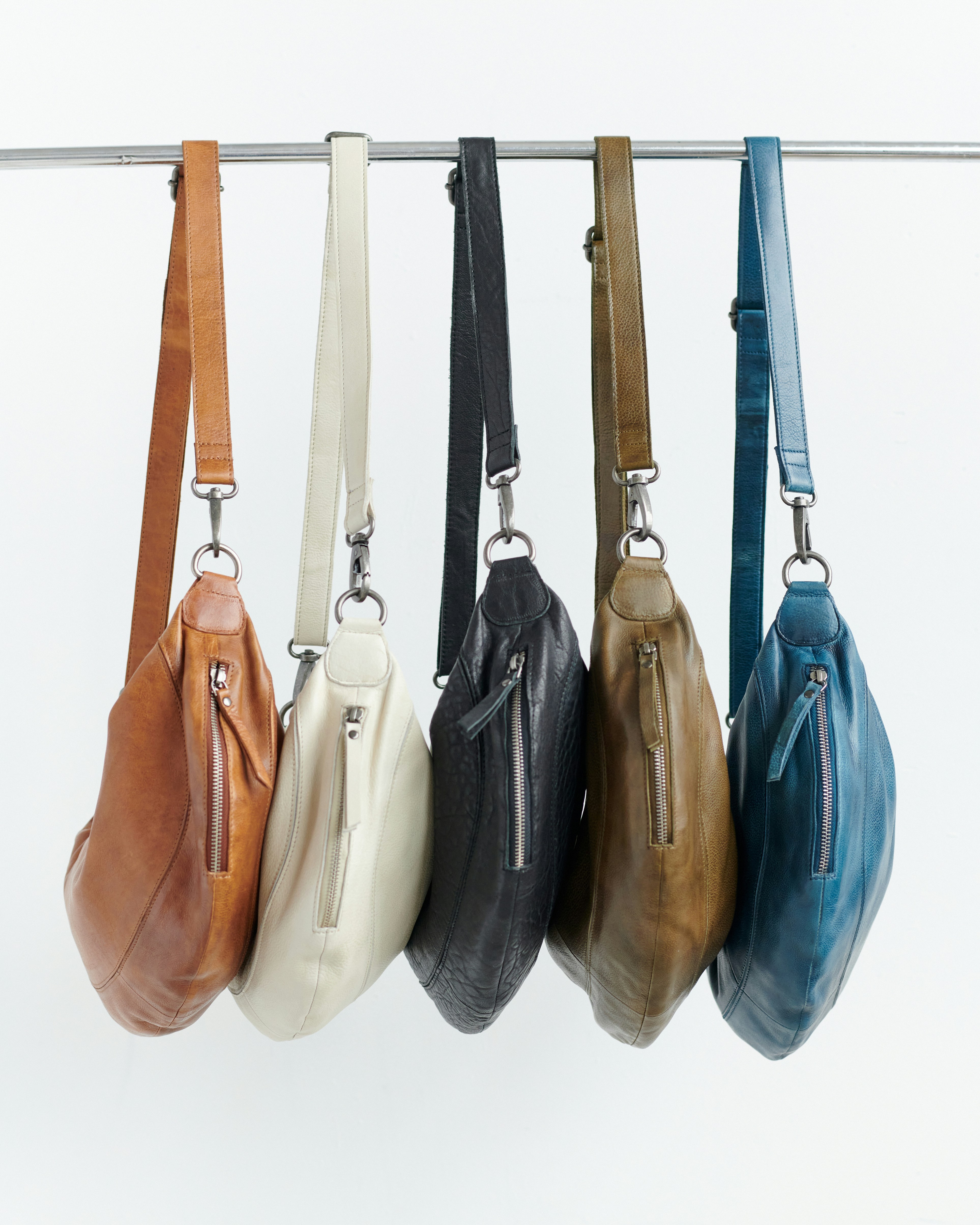 Five leather crossbody bags in different colors hanging.