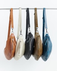 Five leather crossbody bags in different colors hanging.