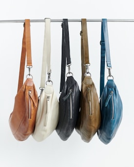 Five leather crossbody bags in different colors hanging.