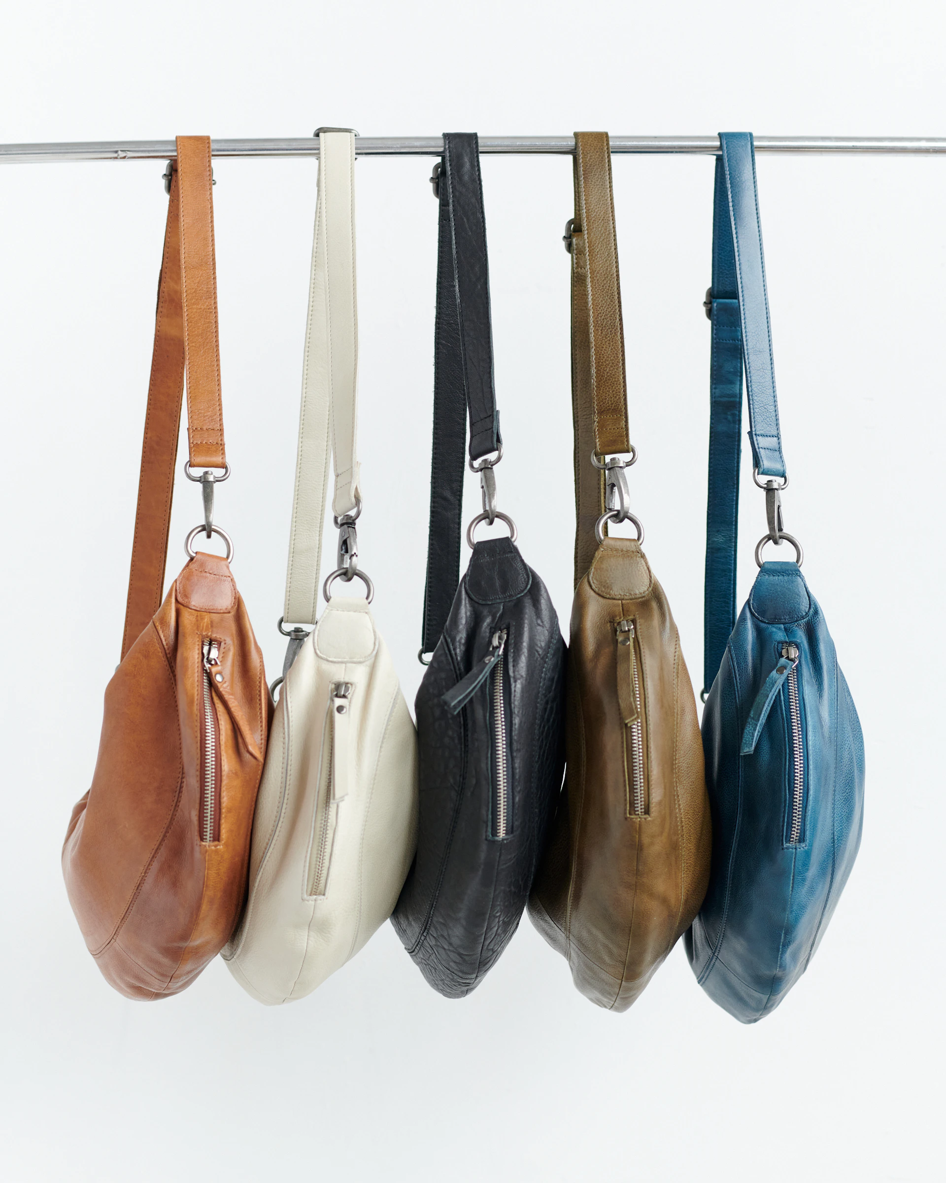Five leather crossbody bags in different colors hanging.