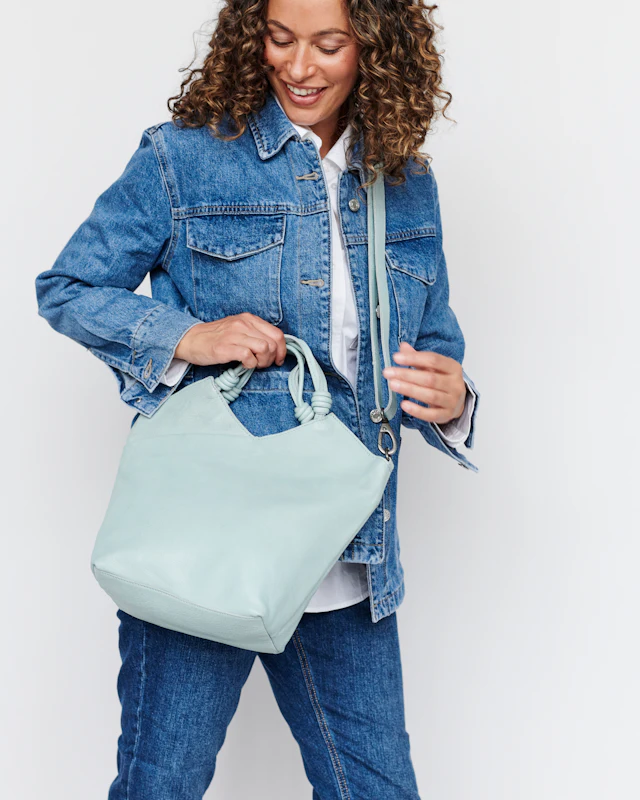 A woman in a denim jacket holding a light blue handbag