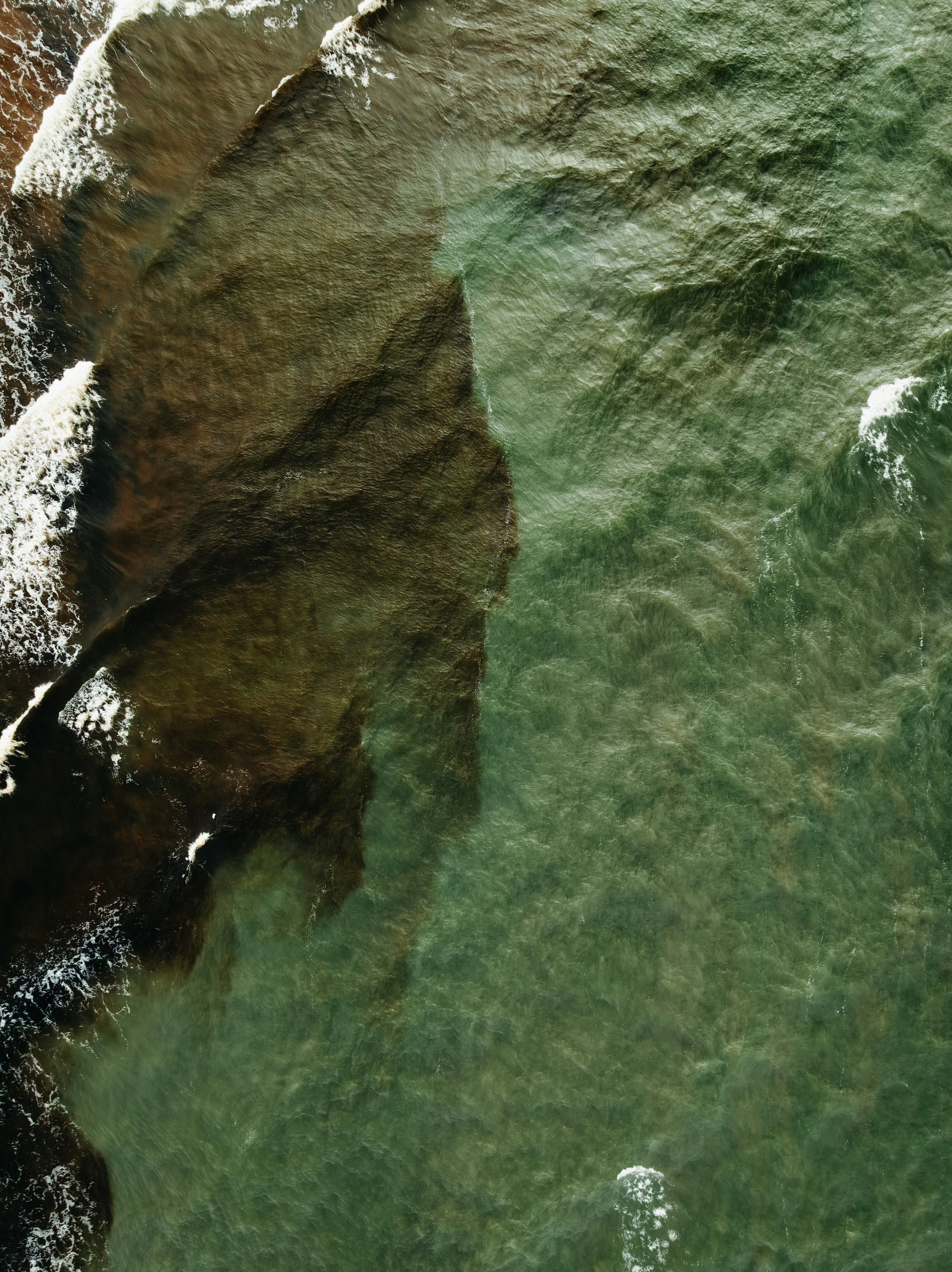Aerial view of rocky shore meeting green ocean waves