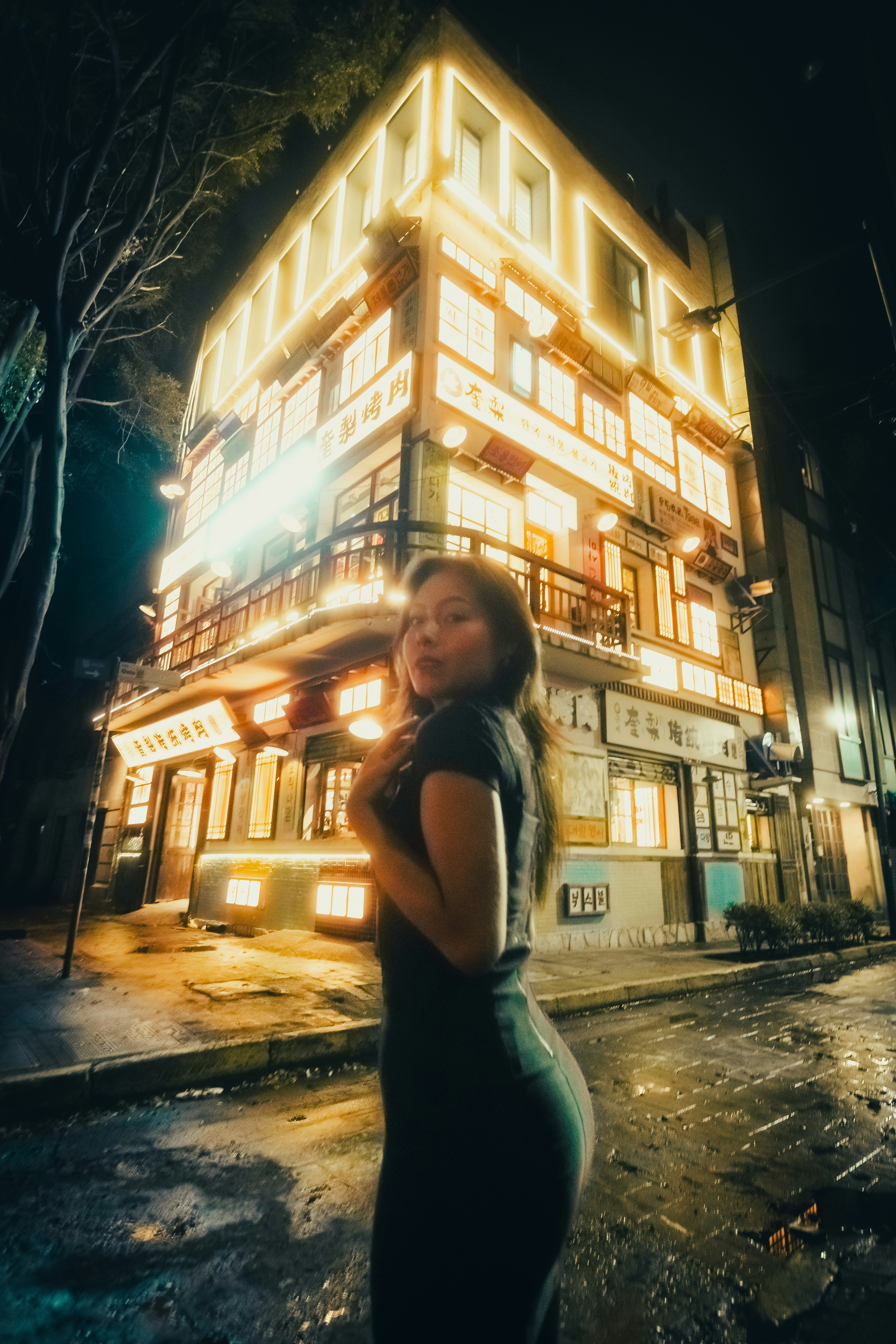 Woman poses in front of brightly lit building at night