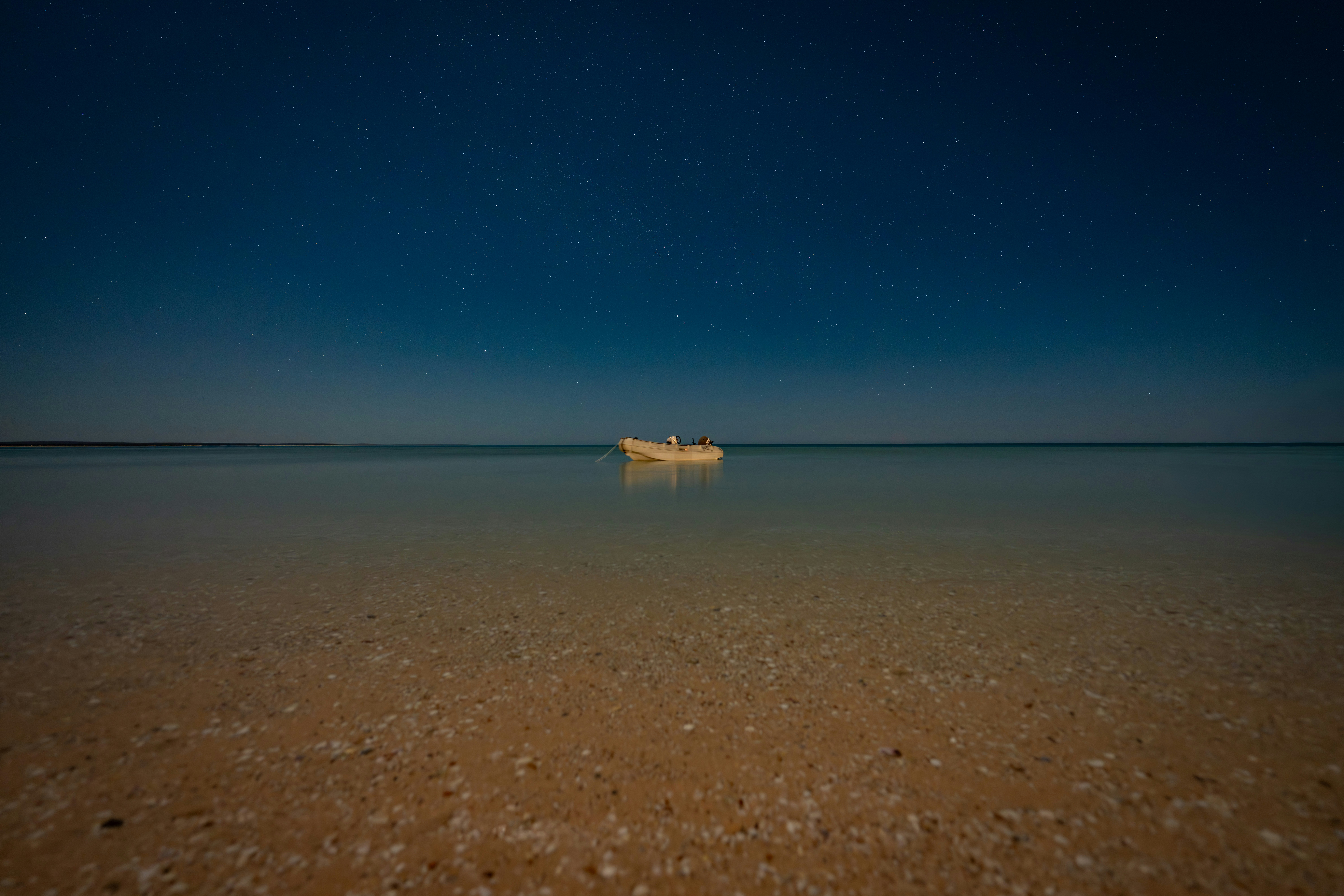 A small boat floats on a calm sea under stars.