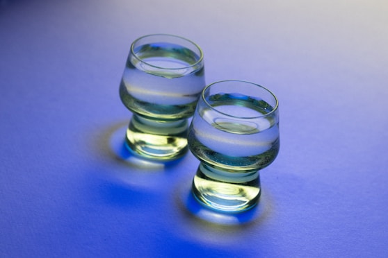 Two glasses of clear liquid on blue surface