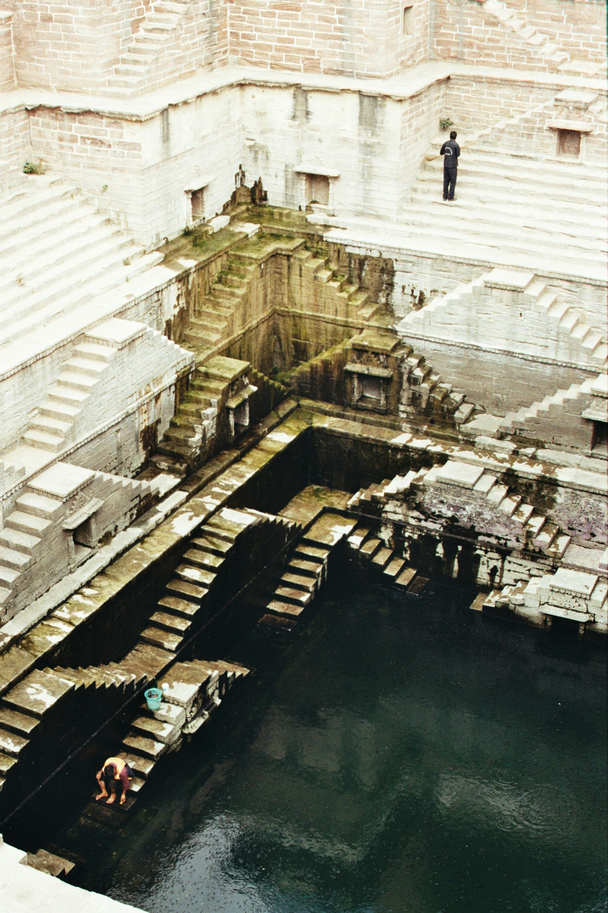 Intricate steps descend into a deep well with dark water.