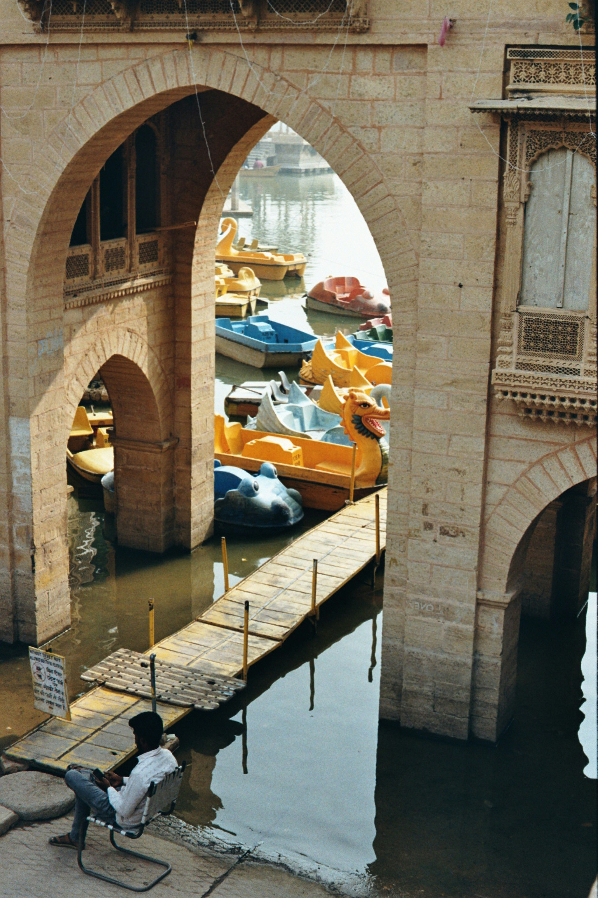 Man sits by arches overlooking boats on water