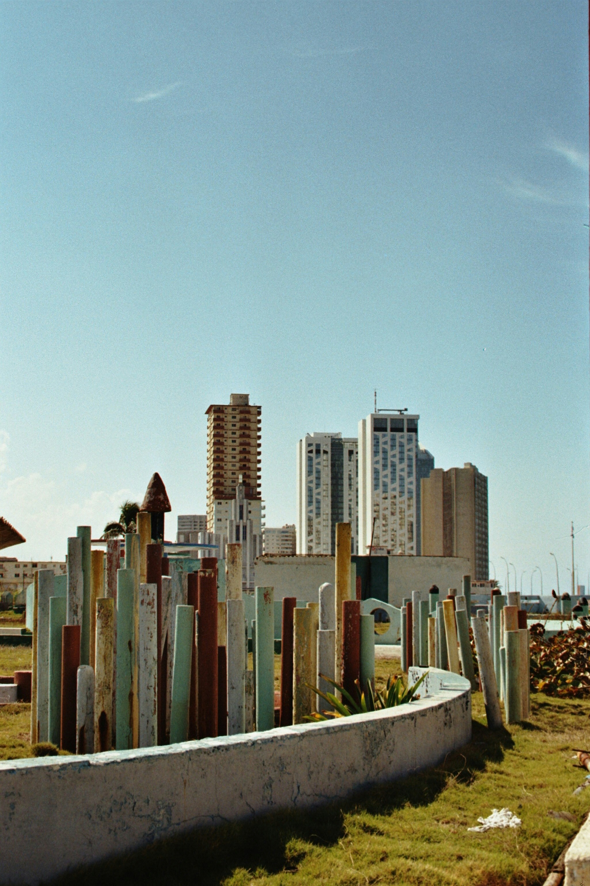 Colorful wooden posts in a park with city buildings behind.