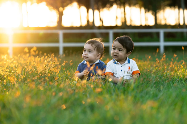 Two babies sitting in grassy field at sunset