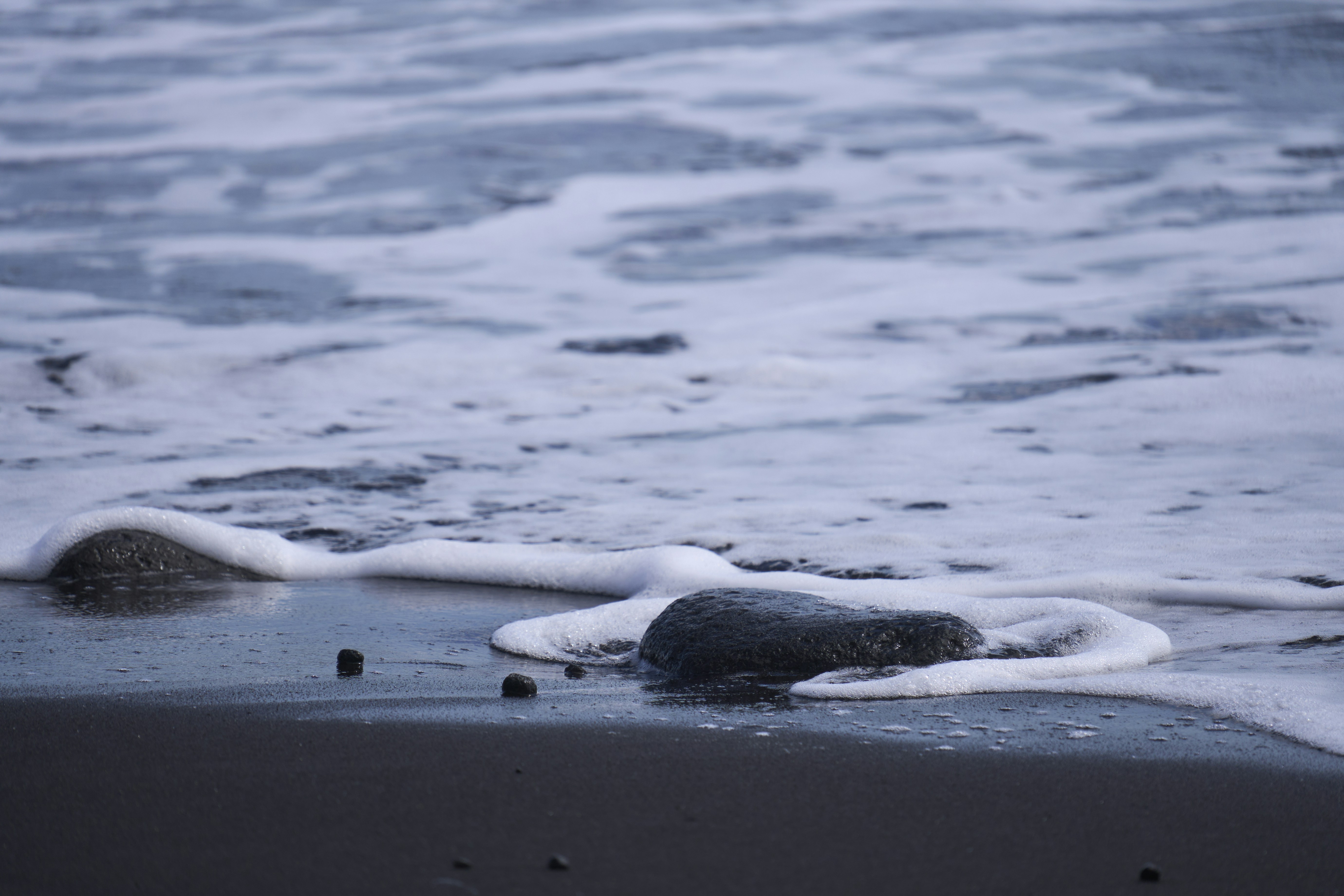 Waves washing over rocks on a dark beach