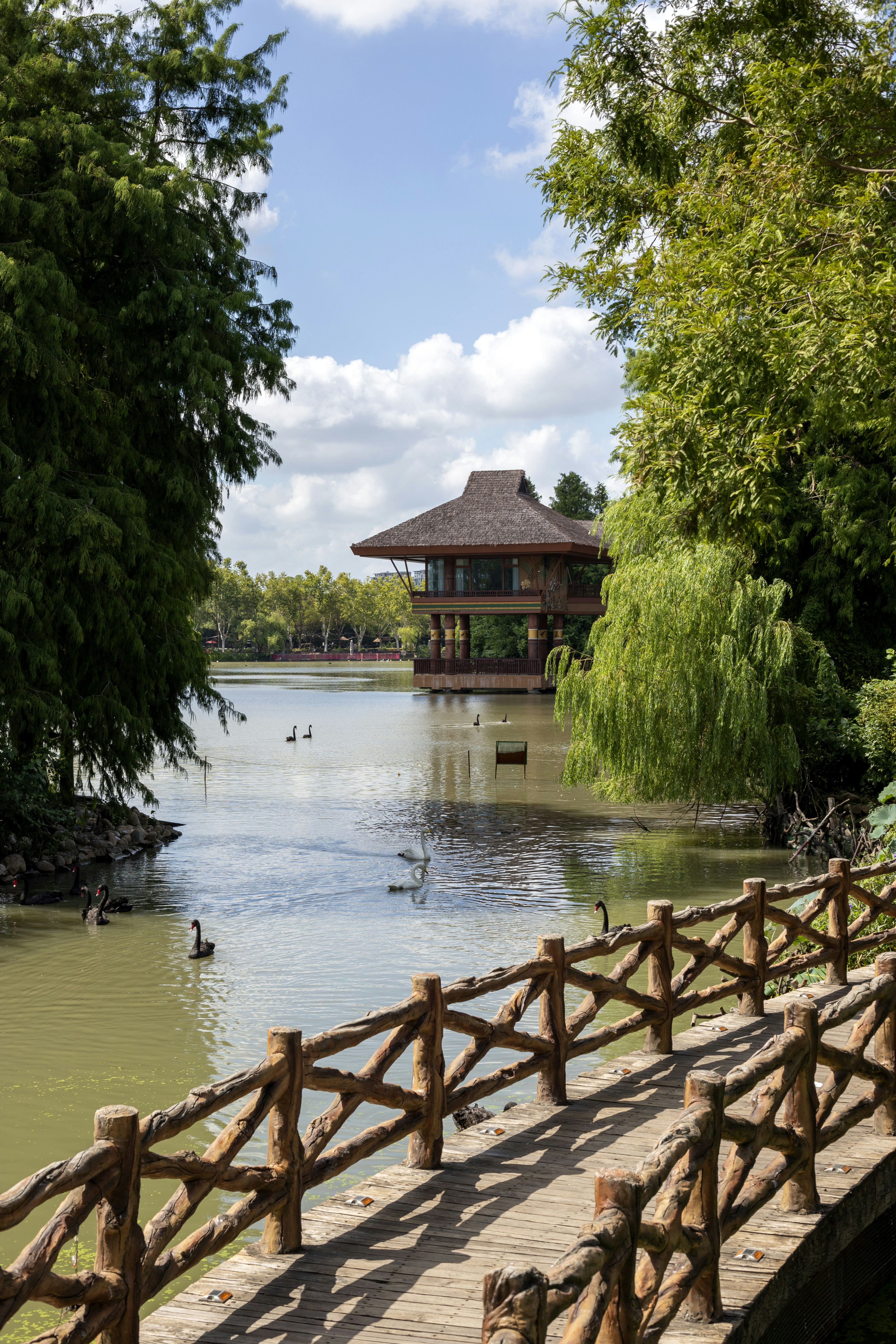 Wooden bridge leads to a tranquil lake with pavilion.
