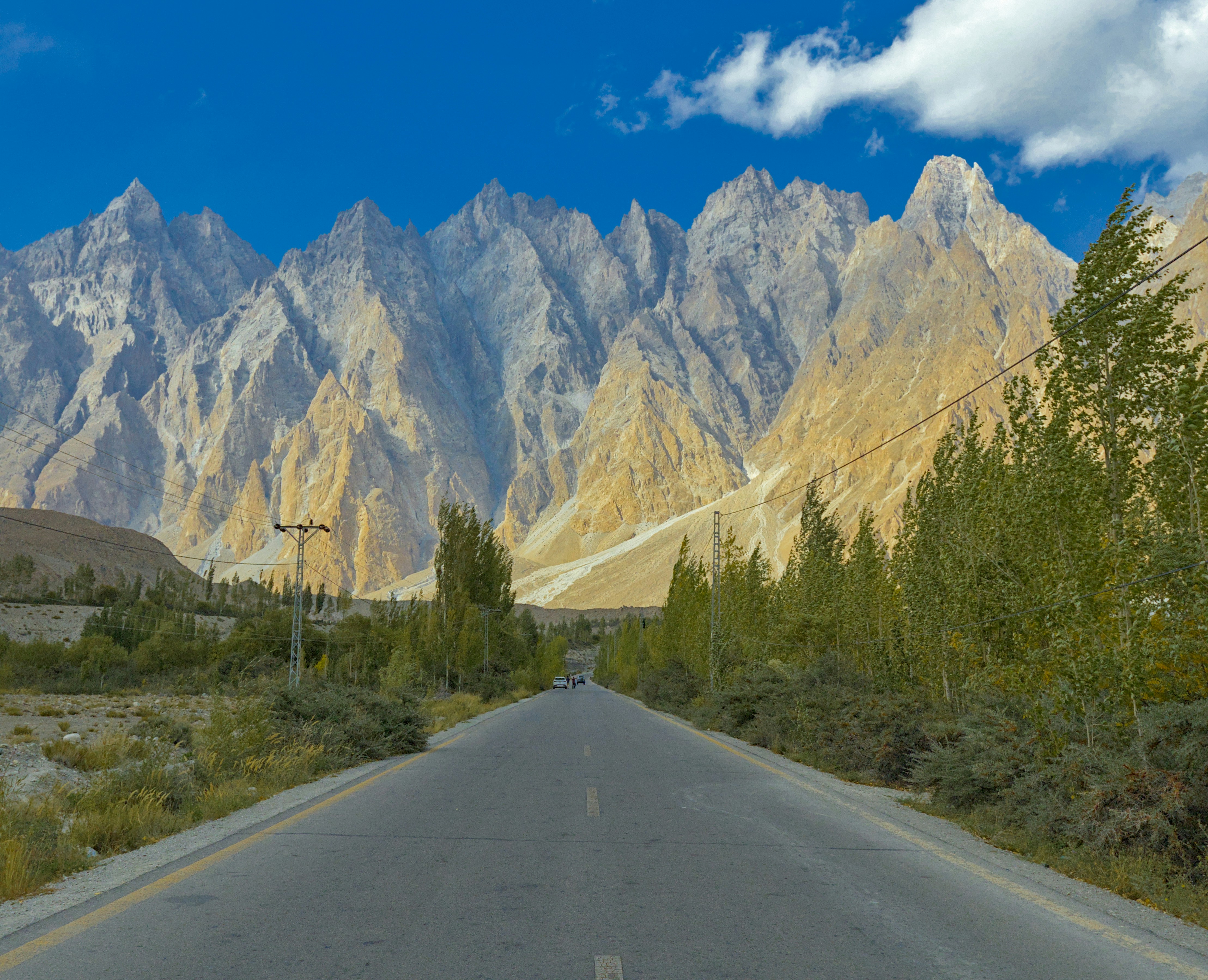 A road leads to jagged mountains under a blue sky.